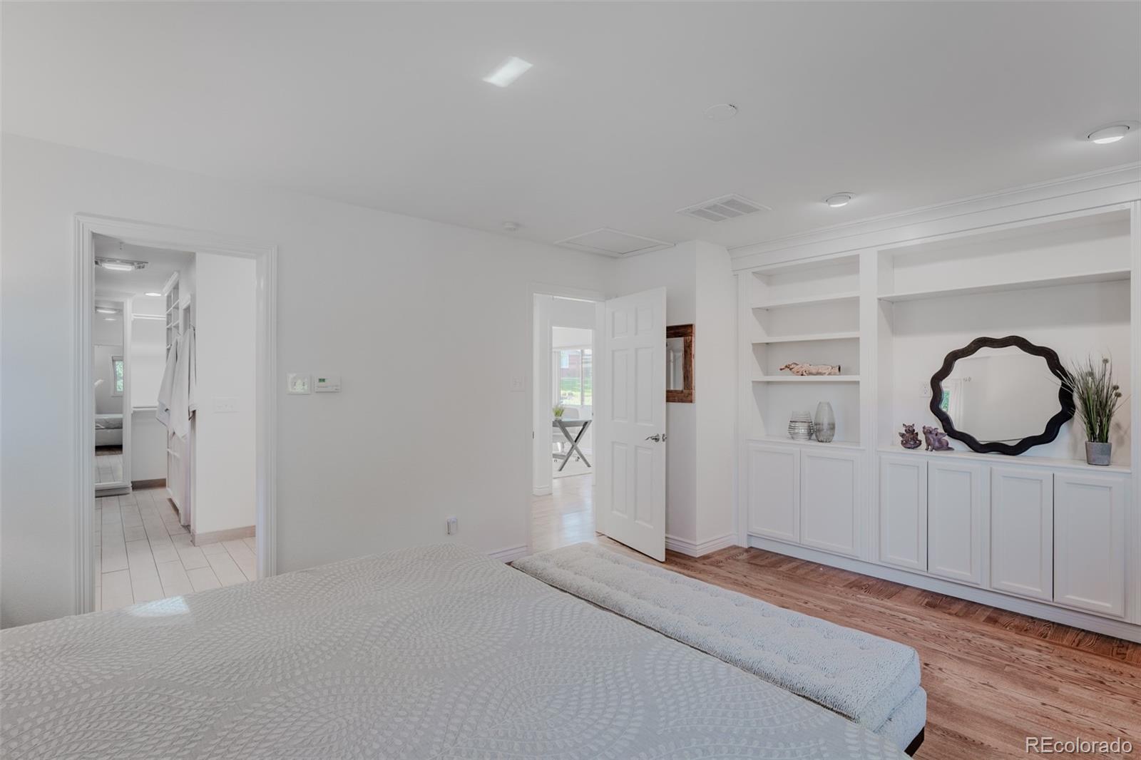 The primary bedroom beckons with its elegant hardwood floors and custom cabinetry, featuring built-in bookshelves that surround a dedicated spot for a TV, creating a perfect blend of allure and functionality.