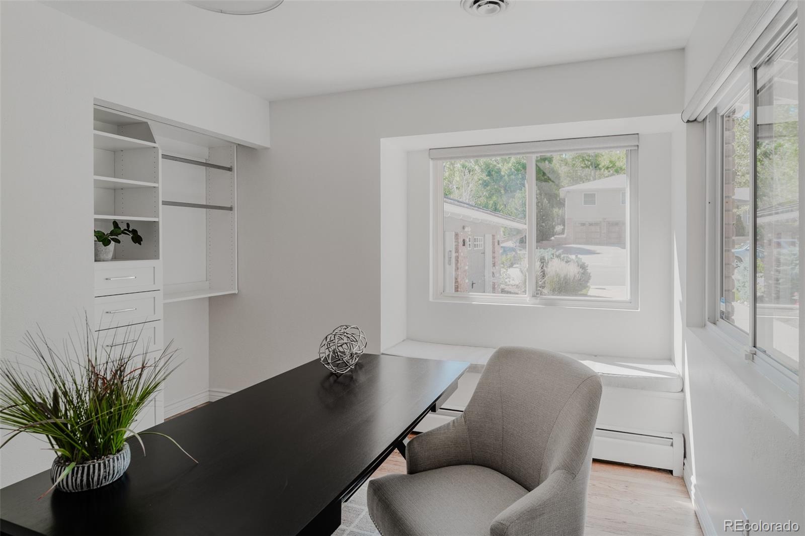 The main level secondary bedroom, designed for versatility, easily doubles as a home office, featuring built-in shelving, ample natural light, and a quiet ambiance ideal for both rest and productivity.