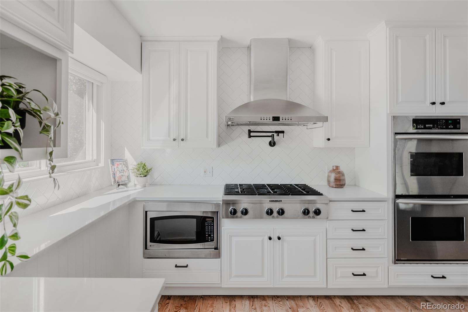 The kitchen exudes modern elegance with its clean, white cabinetry, open glass-front cabinets, and herringbone set subway tile backsplash.