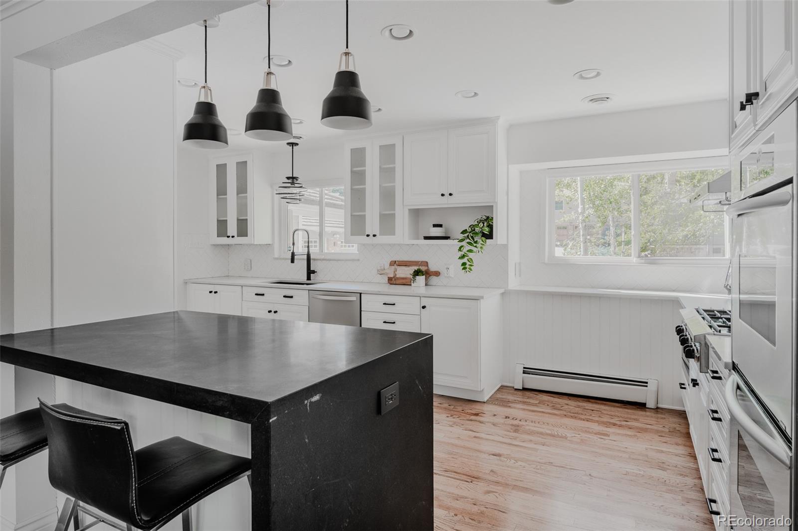 Bold, contrasting black fixtures provide a striking accent, while the substantial honed black quartz waterfall peninsula, paired with stylish light fixtures, elevates the space’s sophistication.