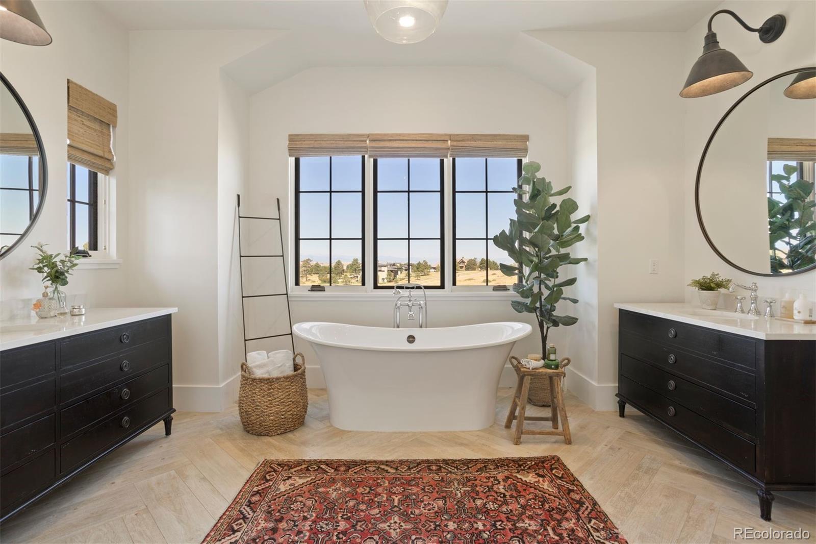 Primary bathroom with freestanding soaking tub, walk-in shower, Restoration Hardware® vanities and mirrors, quartzite countertops, and herringbone-patterned flooring.