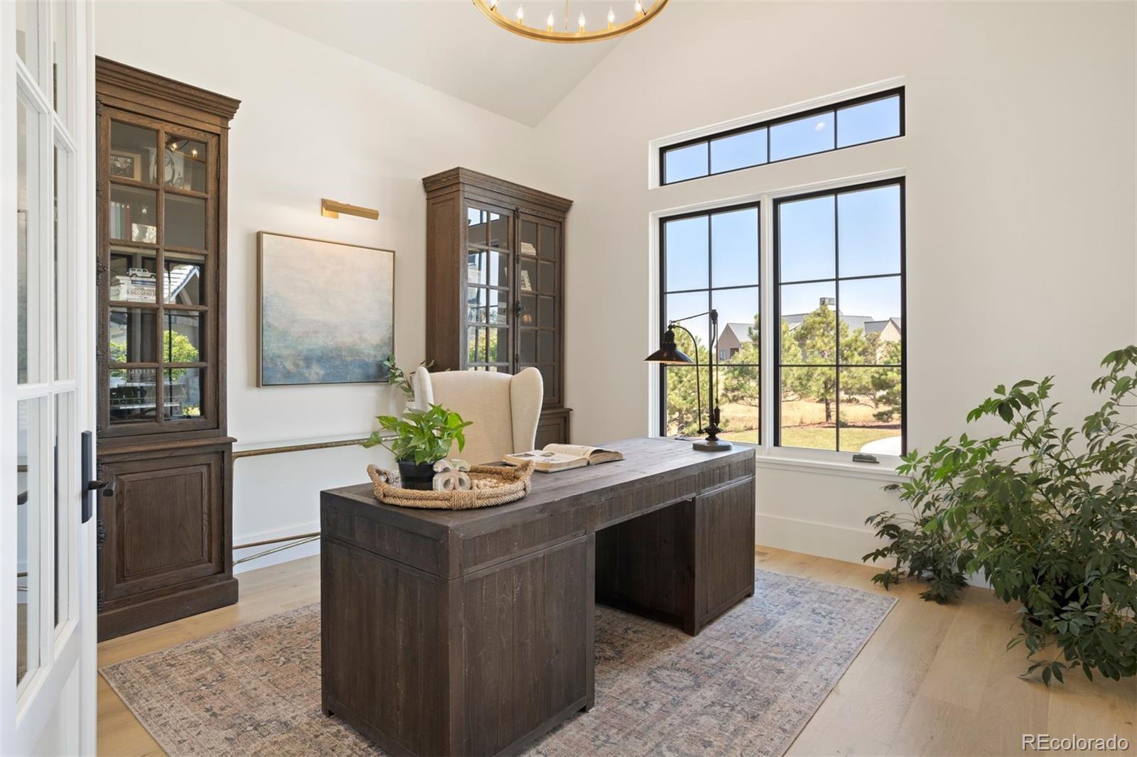 Office on main level with 14-foot vaulted ceiling with brass chandelier, art light, and French door entry.