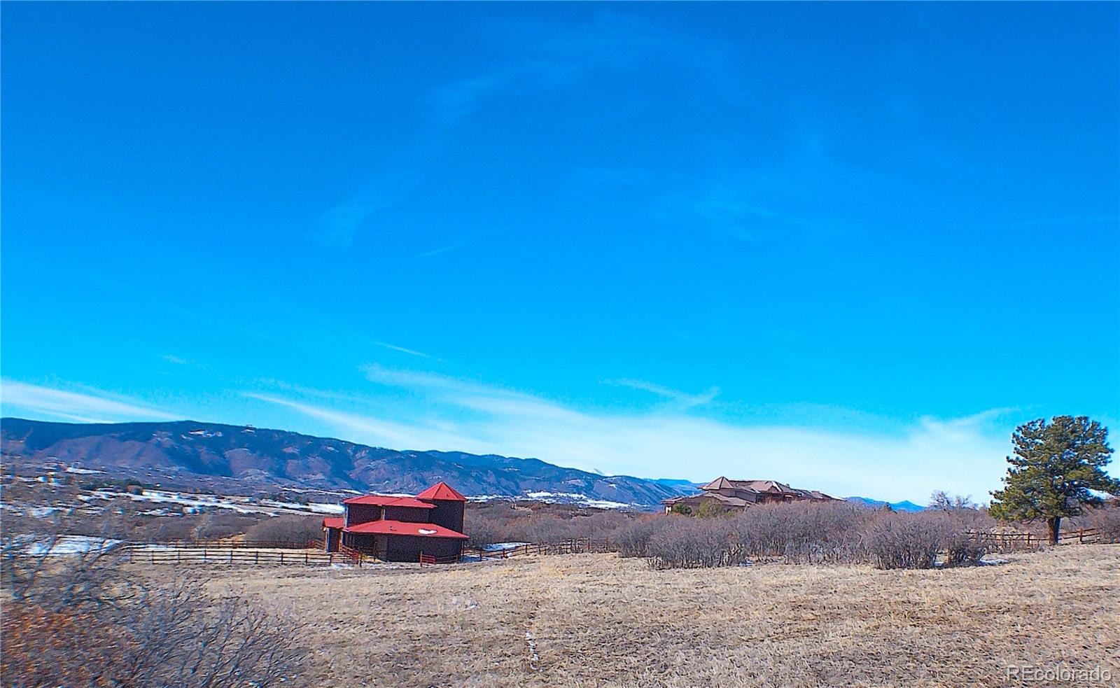 Large and immaculate Barn and corrals with home roofline above.