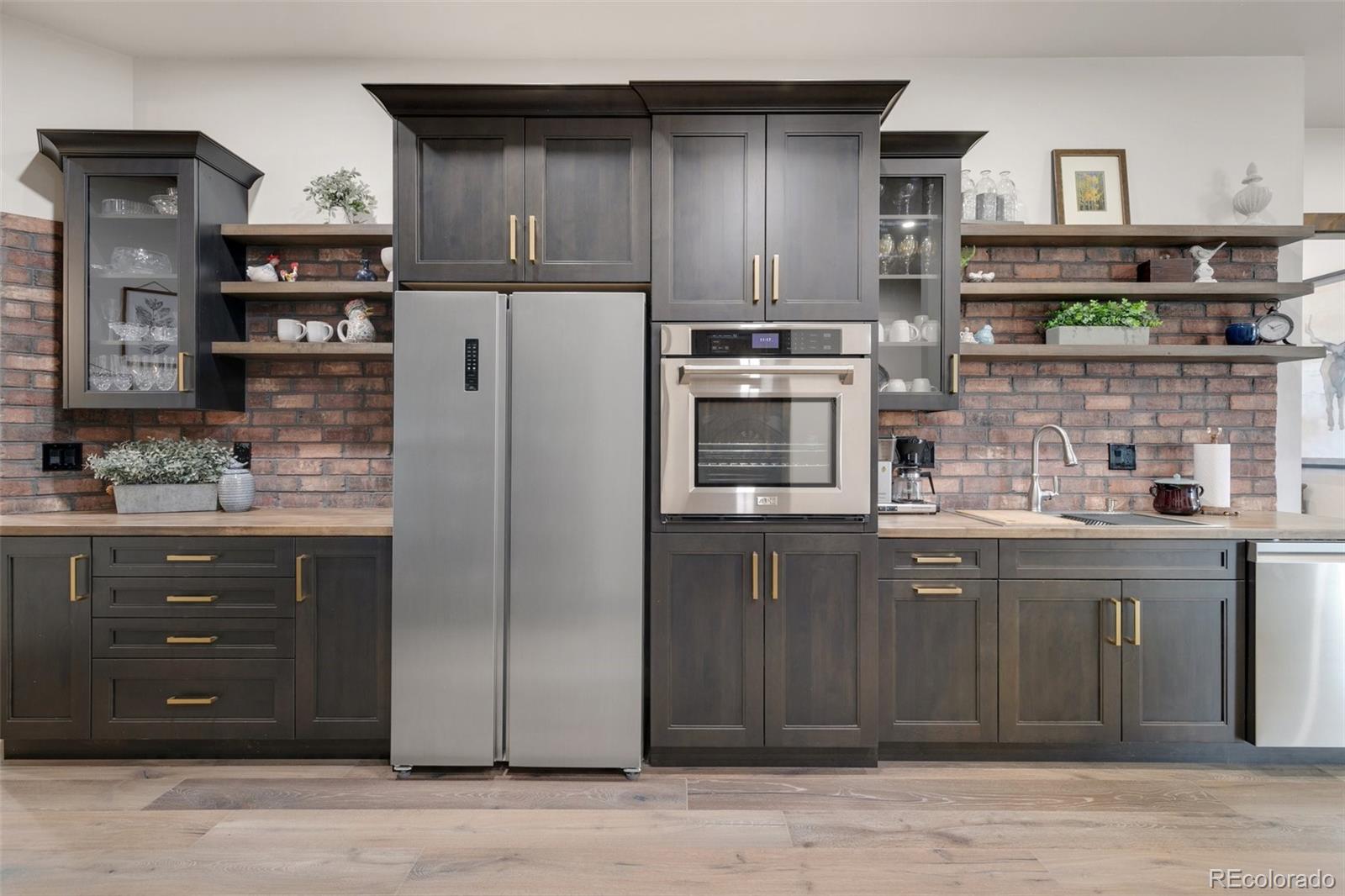 Butlers kitchen with oven, dishwasher, sink, fridge and brick backsplash.