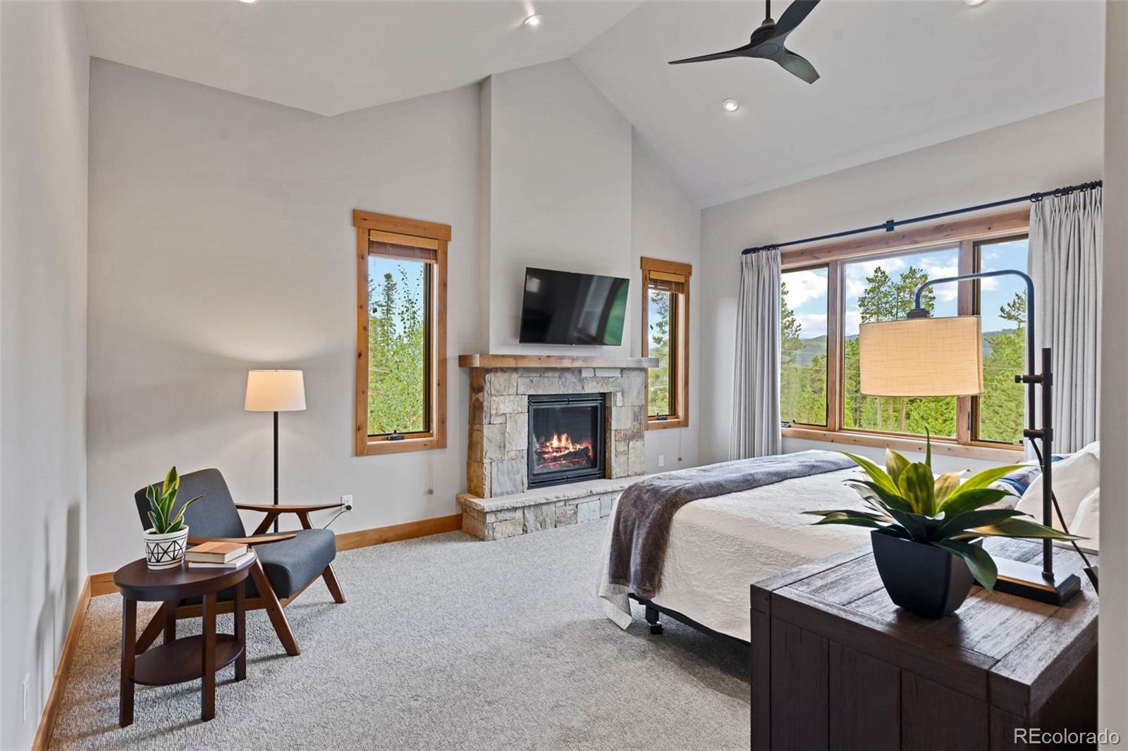 Primary bedroom with forested views and a stone surround fireplace