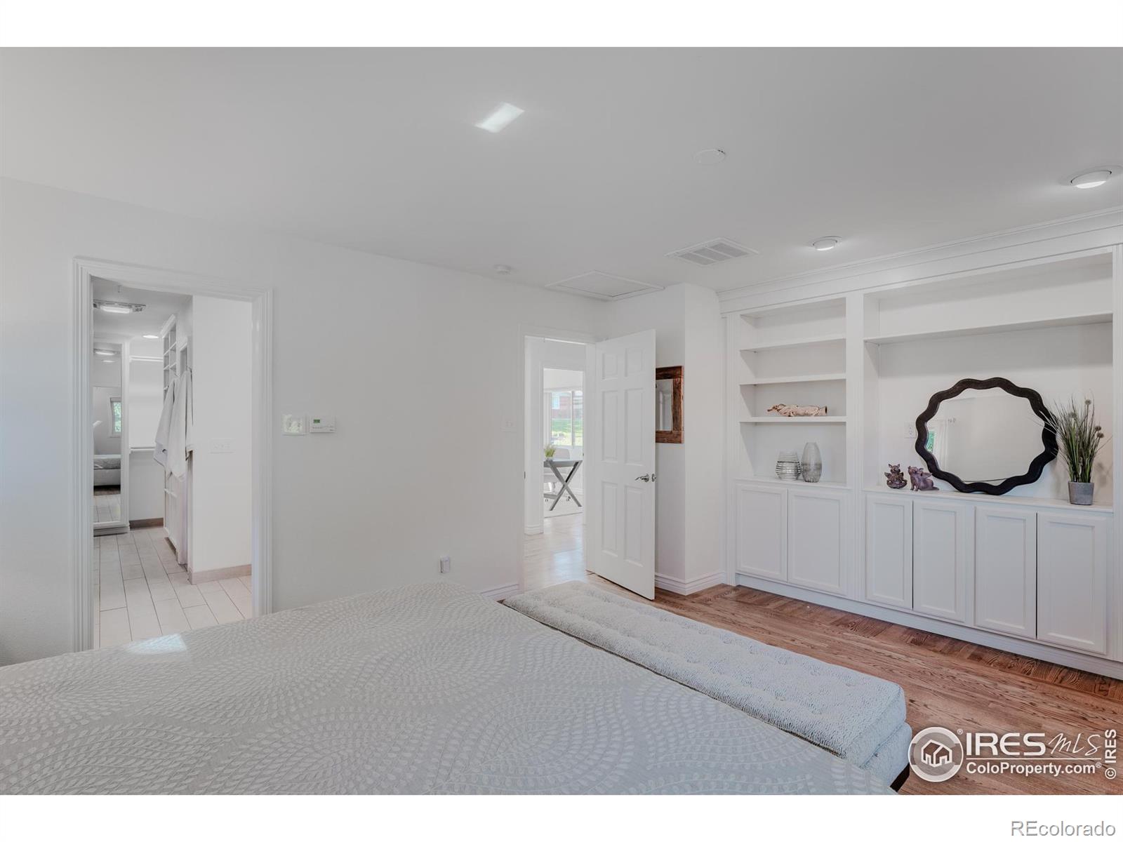 The primary bedroom beckons with its elegant hardwood floors and custom cabinetry, featuring built-in bookshelves that surround a dedicated spot for a TV, creating a perfect blend of allure and functionality.