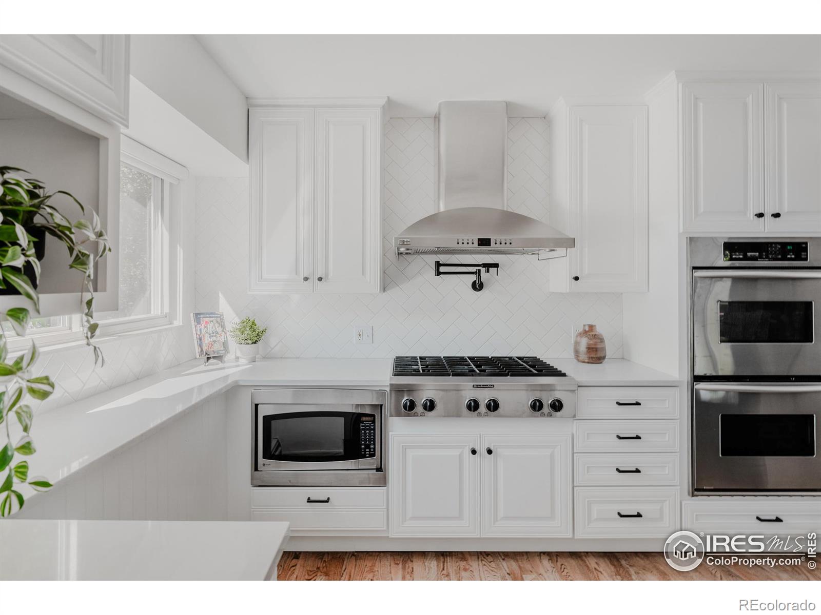 The kitchen exudes modern elegance with its clean, white cabinetry, open glass-front cabinets, and herringbone set subway tile backsplash.