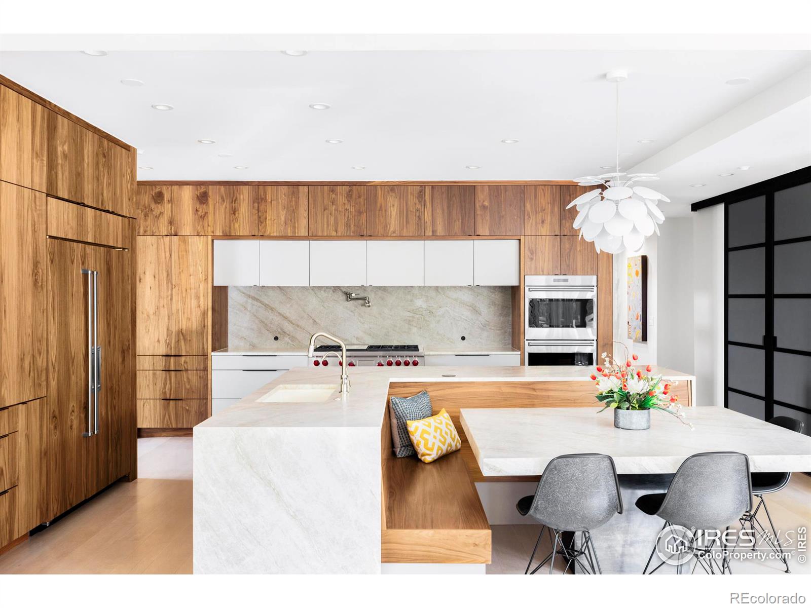 The work-of-art kitchen impresses with custom floor-to-ceiling walnut cabinetry, honed Taj Mahal quartzite countertops, and a large pantry behind smoked-glass barn doors.