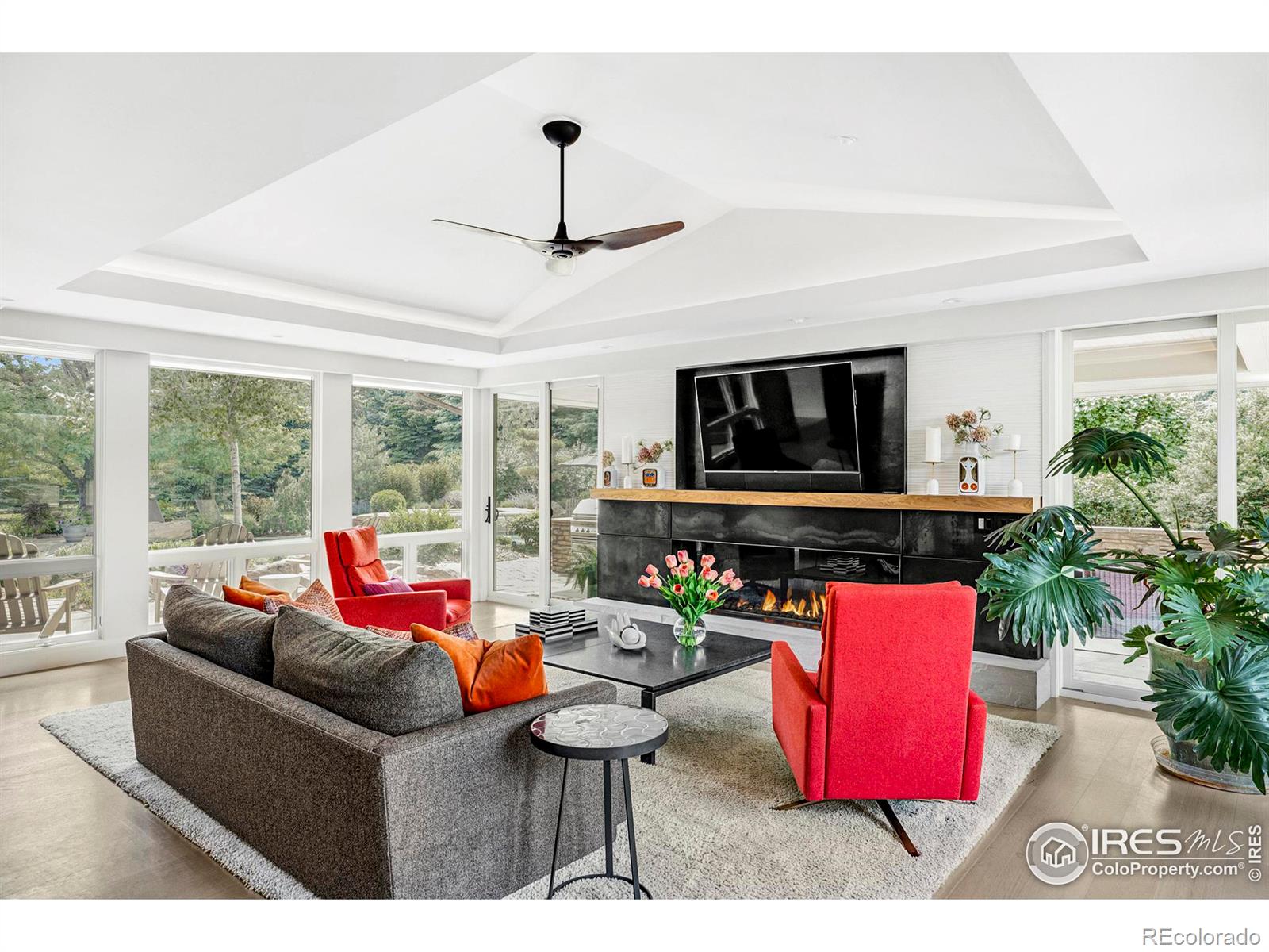 Long linear fireplace, triple exposures, and dual sliding glass doors creating a seamless connection to the manicured landscape, pool, and outdoor living room and kitchen.