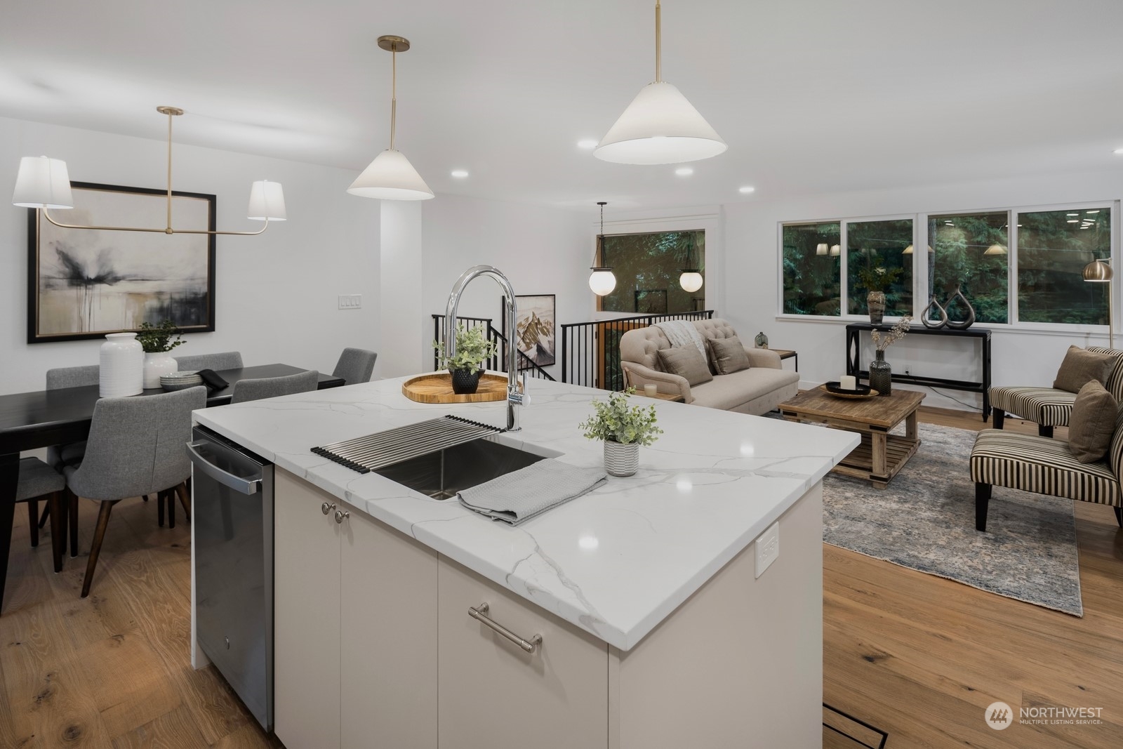 Island with bar seating, quartz countertop, sink and dishwasher, trash can base cabinet, and additional row of base cabinets under bar sitting area.