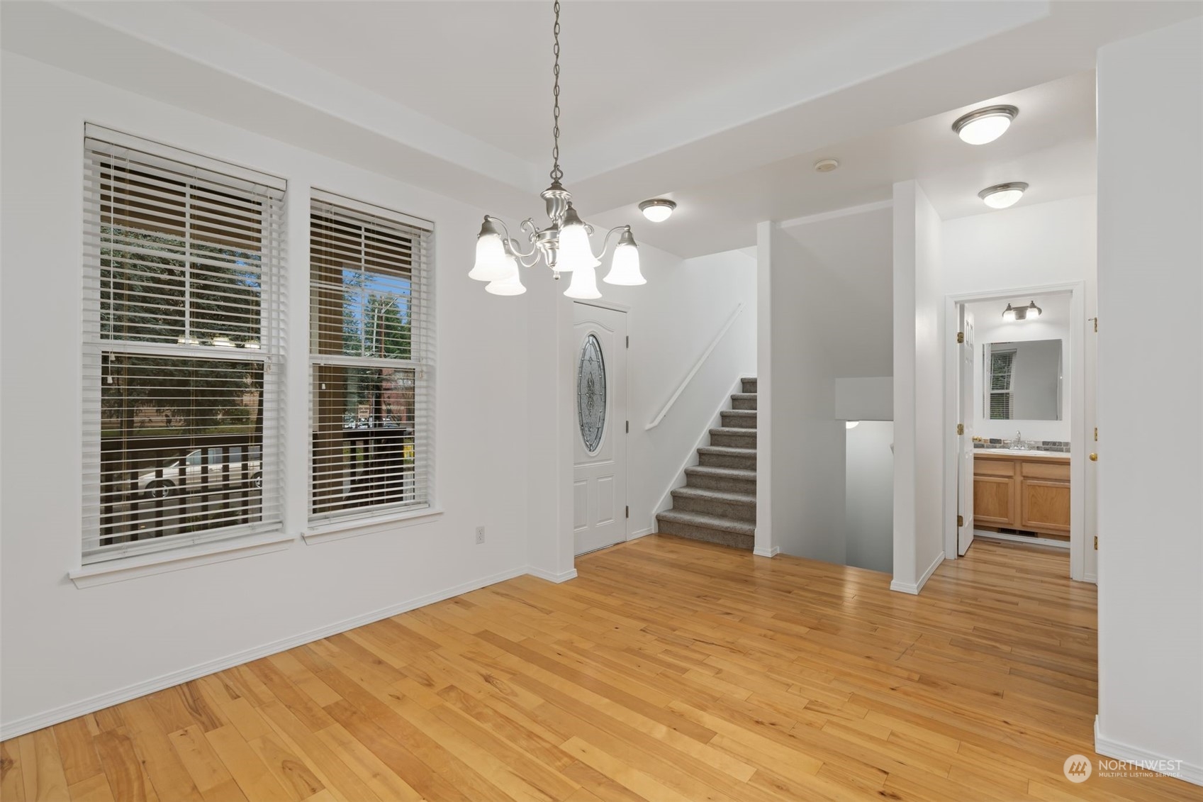 Bright and inviting living area showcasing the stairway leading to the second floor, an adjacent stairway to the basement, and convenient access to the main floor bathroom