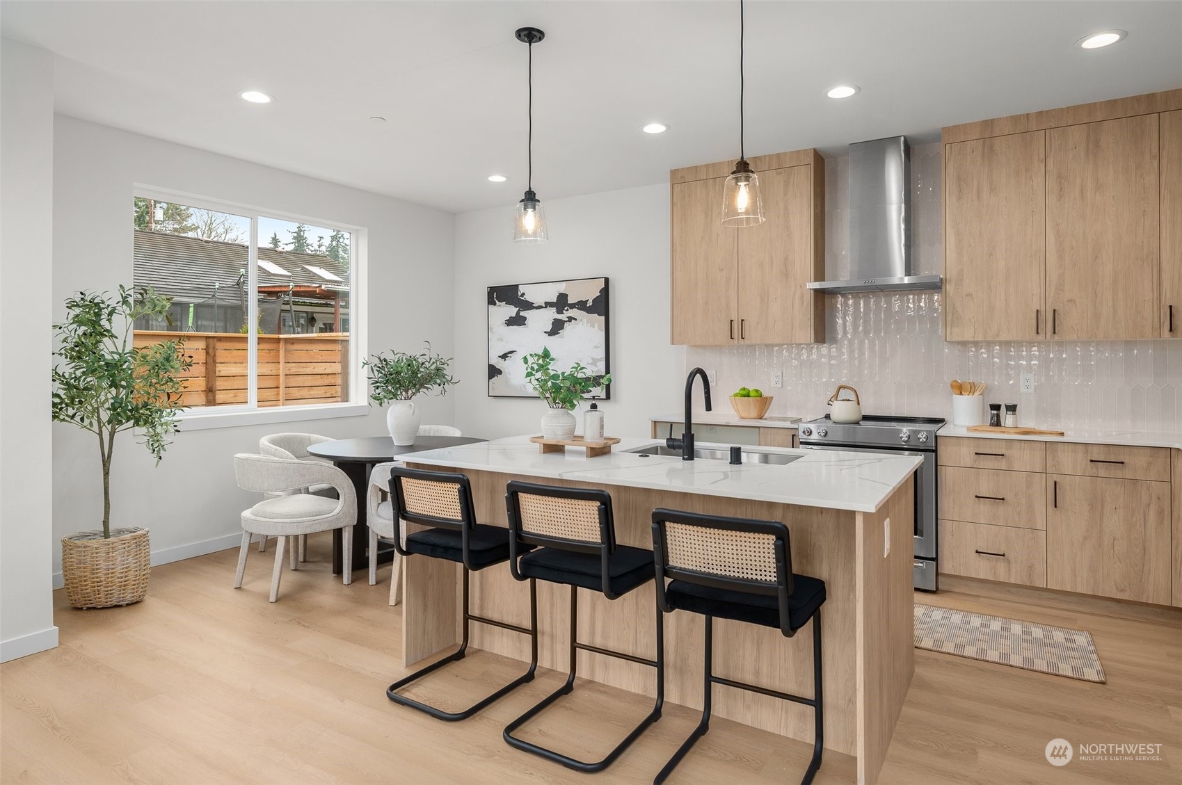 This model home kitchen blends simplicity with modern function. A waterfall quartz island anchors the space, offering room for casual dining, while matte black fixtures and warm wood cabinetry create a striking contrast.