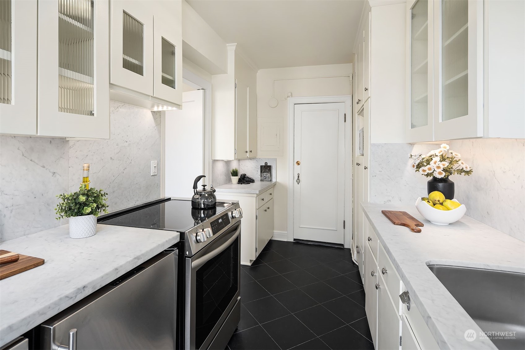 The galley kitchen has been updated with lovely black stone tile, Carrera marble countertops, new stove and dishwasher. Shown here is the "back door" that leads to the common area hallway.