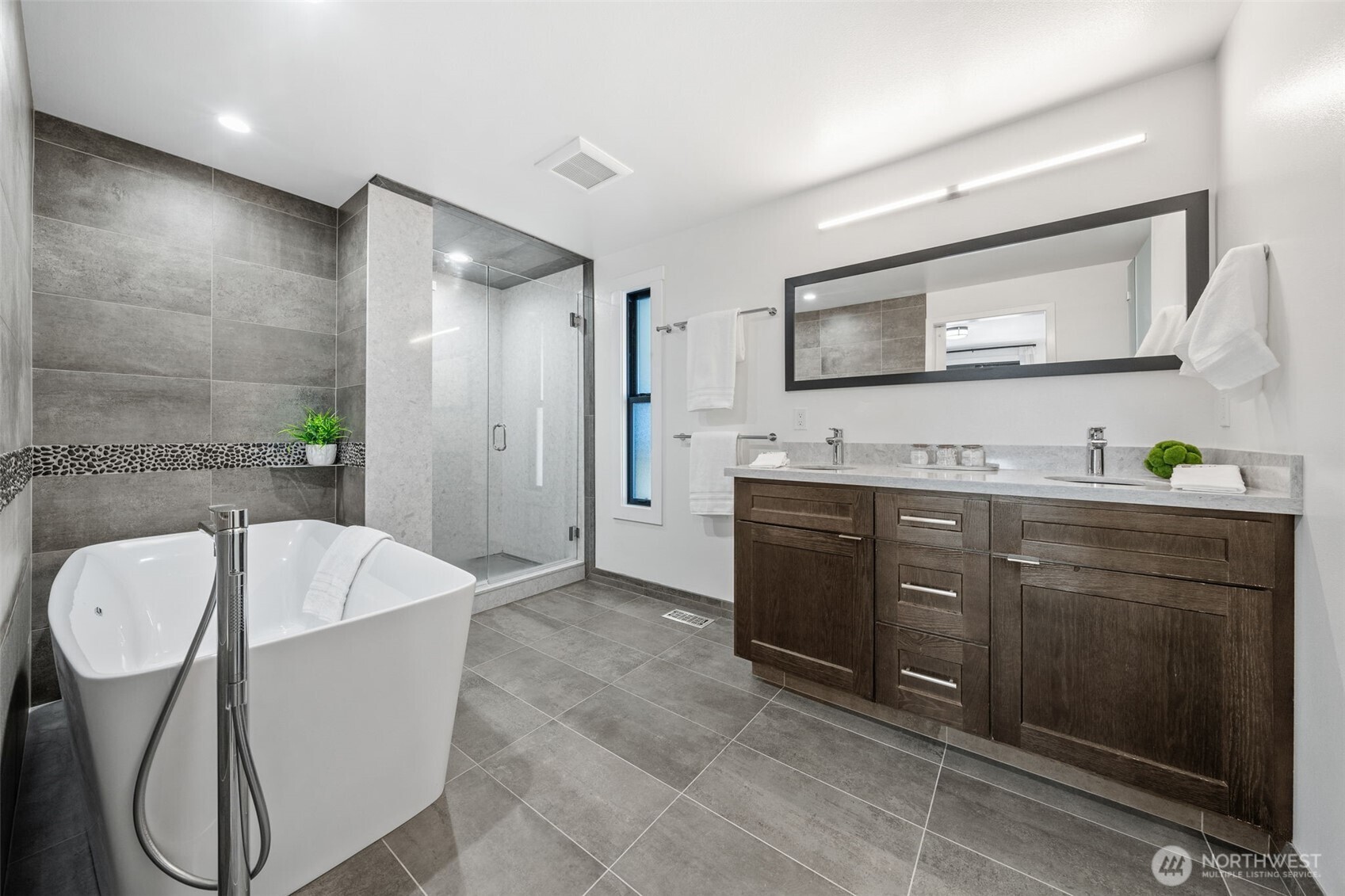 Experience ultimate relaxation in this spa-inspired Primary bath, featuring a freestanding soaking tub with Hansgrohe fixture, a sleek glass-enclosed shower, and elegant dual vanities with modern finishes.