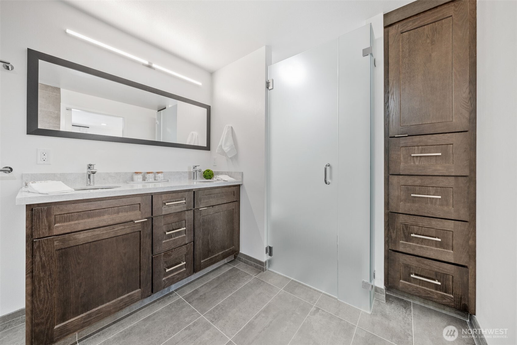 This Primary bath boasts a spacious dual vanity with ample storage, a large framed mirror, and a frosted glass door for added privacy.