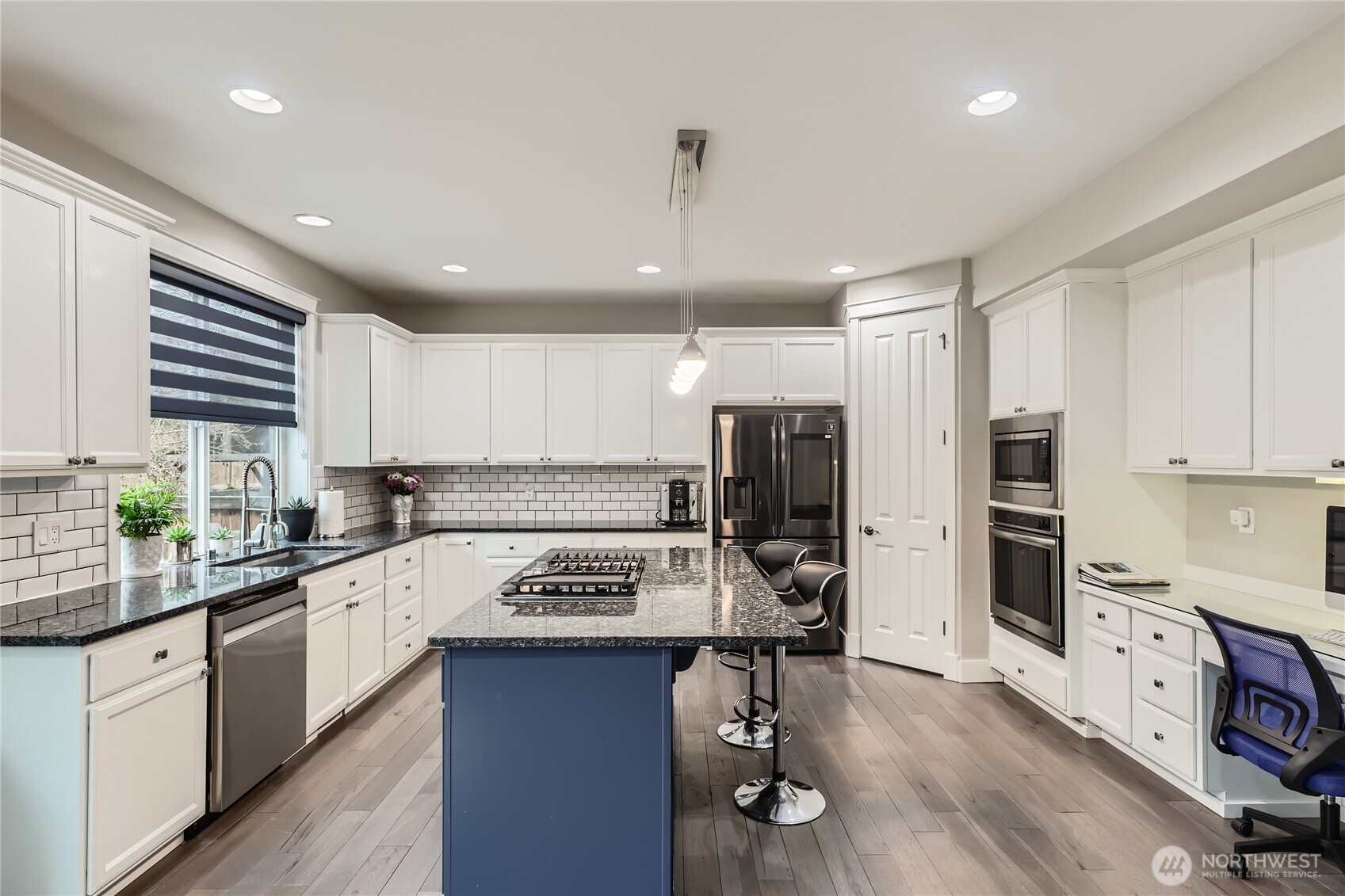 Beautifully updated kitchen showcases white soft-close cabinetry, granite countertops, full-height backsplash, stainless steel appliances, a center island, and planning desk.