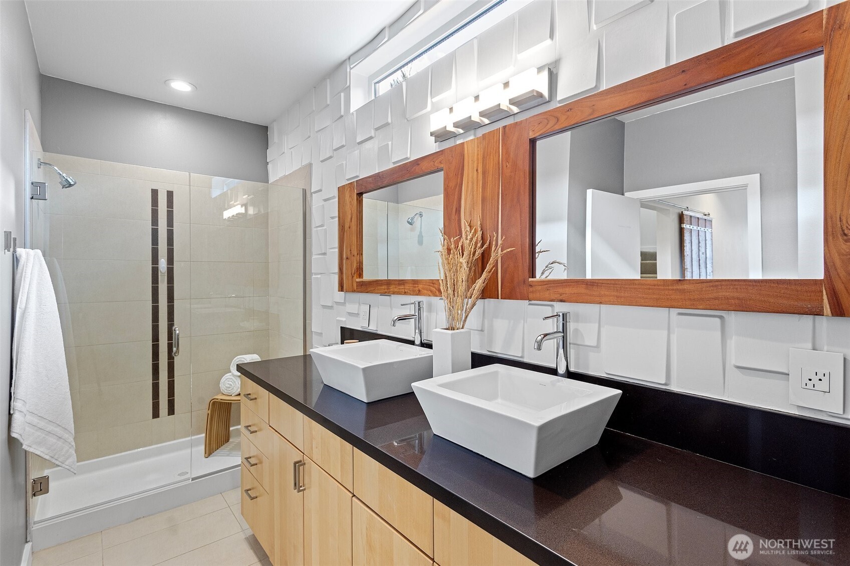 Primary en-suite with large walk-in tiled shower, double vanity with vessel sinks, custom wood trimmed mirrors, tiled flooring and 3D wall paneling.