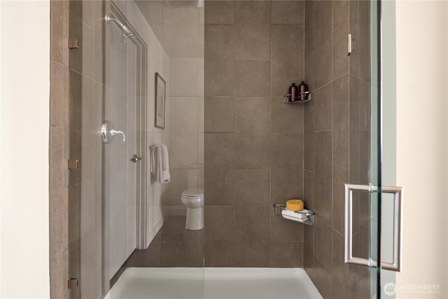 The oversized shower features floor-to-ceiling tile and a frameless glass door.