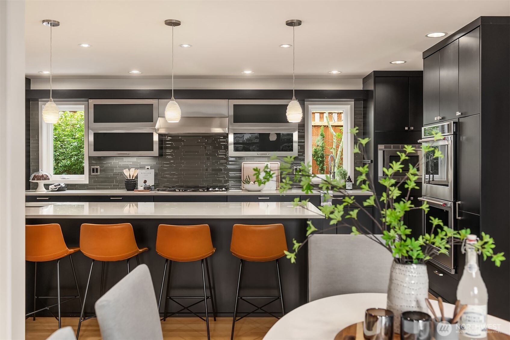 Contemporary kitchen showcases black cabinetry, waterfall island, artisan pendant lighting, and sophisticated linear glass backsplash.