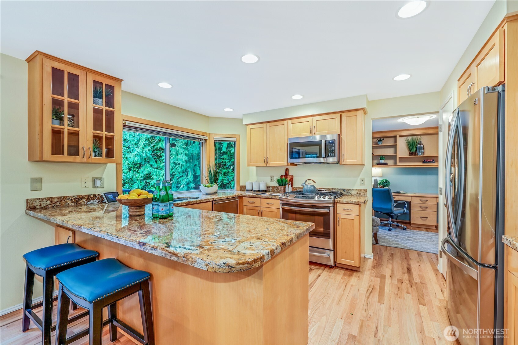 This beautifully updated kitchen features warm wood cabinetry, sleek granite countertops, and refinished hardwood floors. Large windows provide natural light and a serene view of the lush backyard. The stainless steel appliances and gas range offer modern convenience, perfect for home chefs