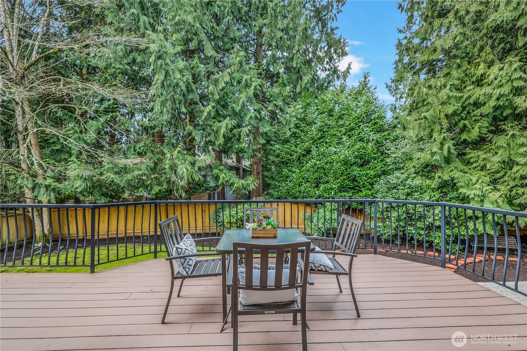 This spacious backyard deck is surrounded by lush greenery, offering a serene and private outdoor retreat. The elevated deck provides an ideal setting for relaxing or entertaining, with a sturdy railing that enhances safety without obstructing the view.