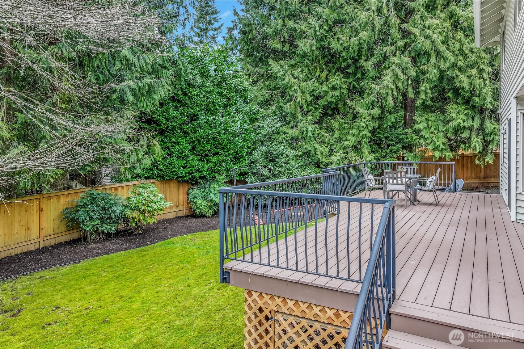 This angle highlights the deck’s easy access to the beautifully landscaped backyard. The black metal railing adds a modern touch, while the warm wood tones of the deck harmonize with the surrounding natural elements.