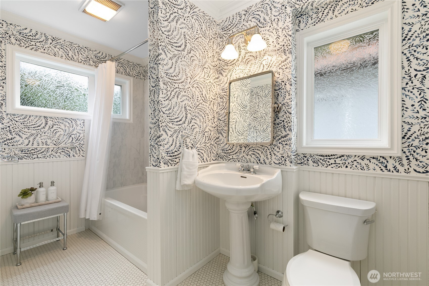 A fresh twist on classic design, this bath features whimsical wallpaper, a timeless pedestal sink, and crisp beadboard paneling. Frosted windows ensure privacy while allowing in soft, natural light. The clean, white tile flooring ties it all together, creating a spa-like retreat that’s both practical and charming.