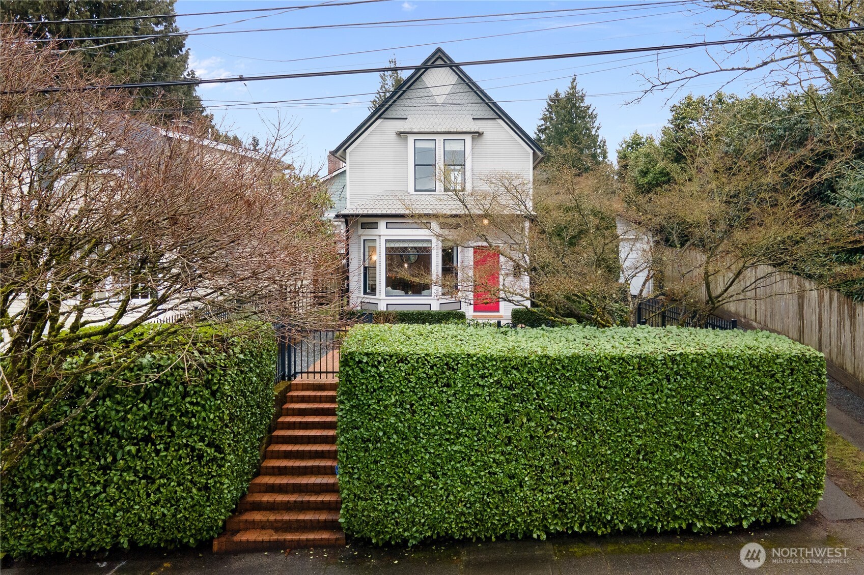 Tucked behind a lush, meticulously trimmed hedge, this front yard offers a blend of privacy and undeniable curb appeal. Brick steps lead to the welcoming porch and striking red door, setting a gracious tone for the home’s interior.