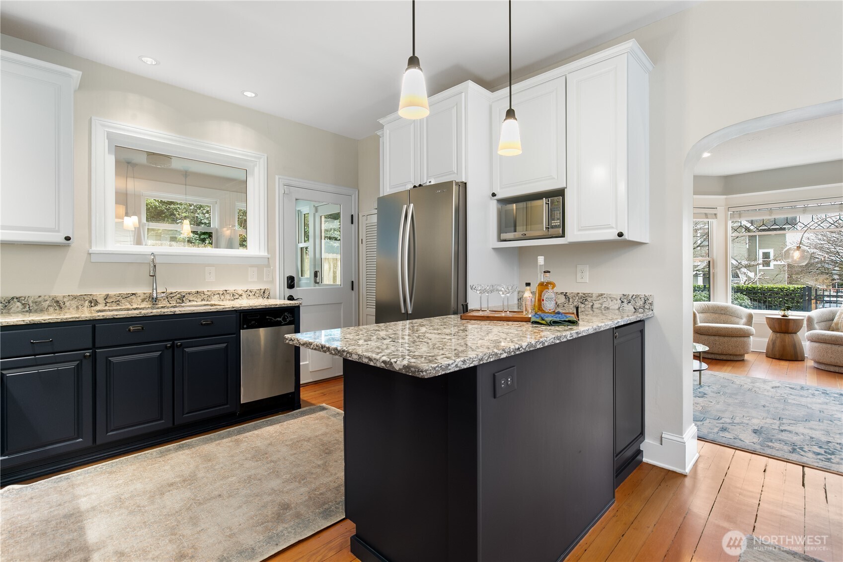 The striking two-tone cabinetry—crisp white uppers and a rich navy island—offers both style and function, while sleek granite countertops and pendant lighting complete the modern aesthetic.