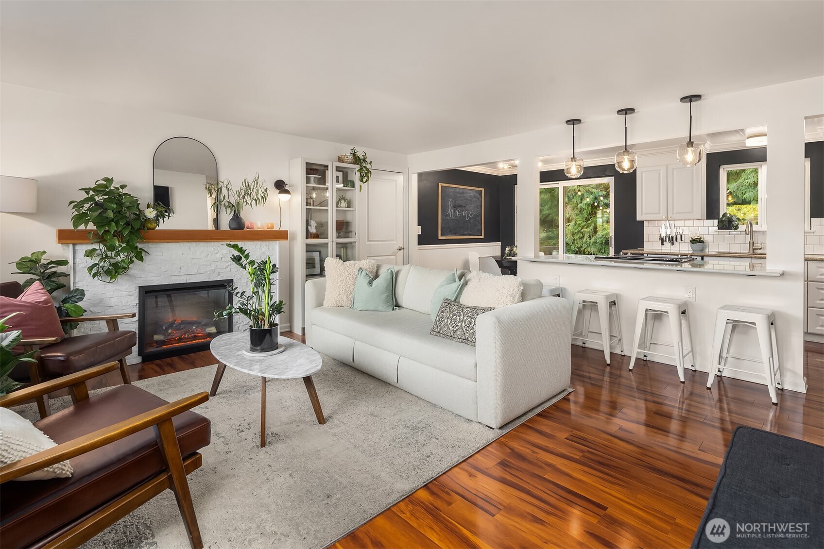 Living room with modern fireplace, wood floors and open concept design leading into the kitchen.