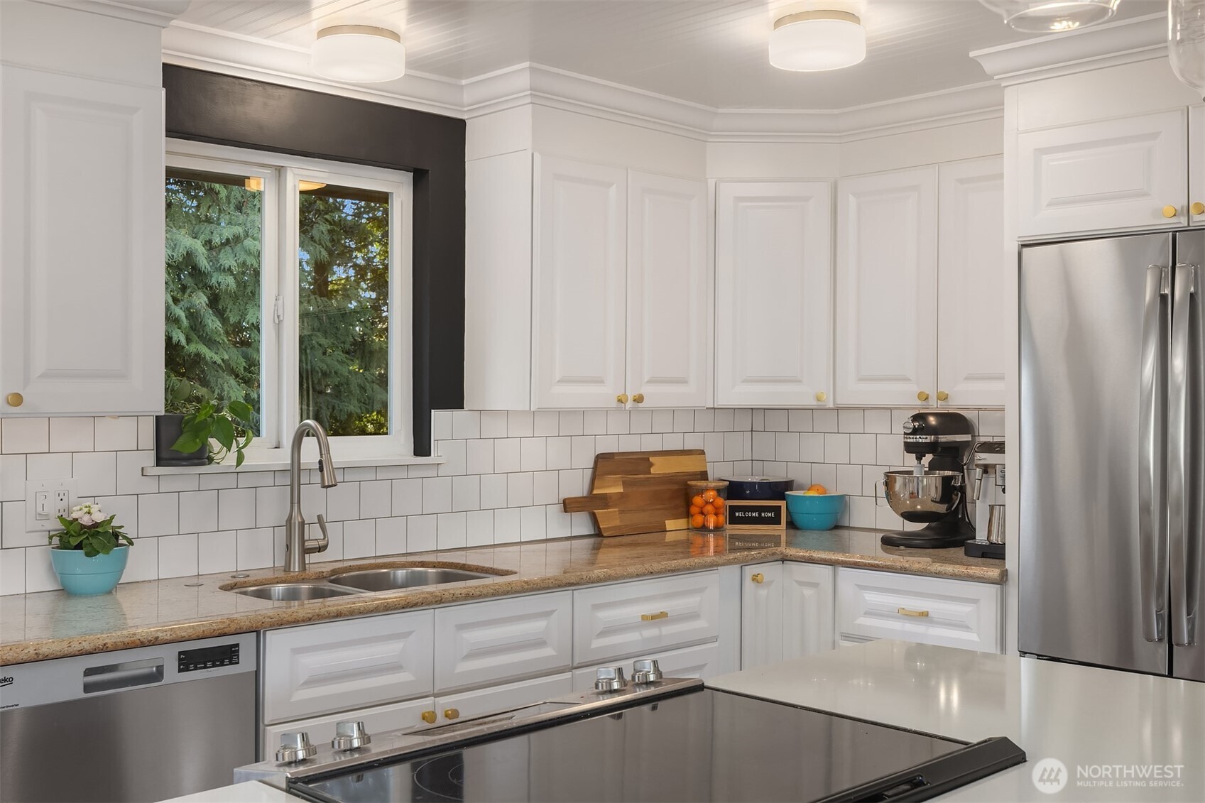 Modern kitchen with white cabinetry, stainless steel appliances and a window letting in natural light.