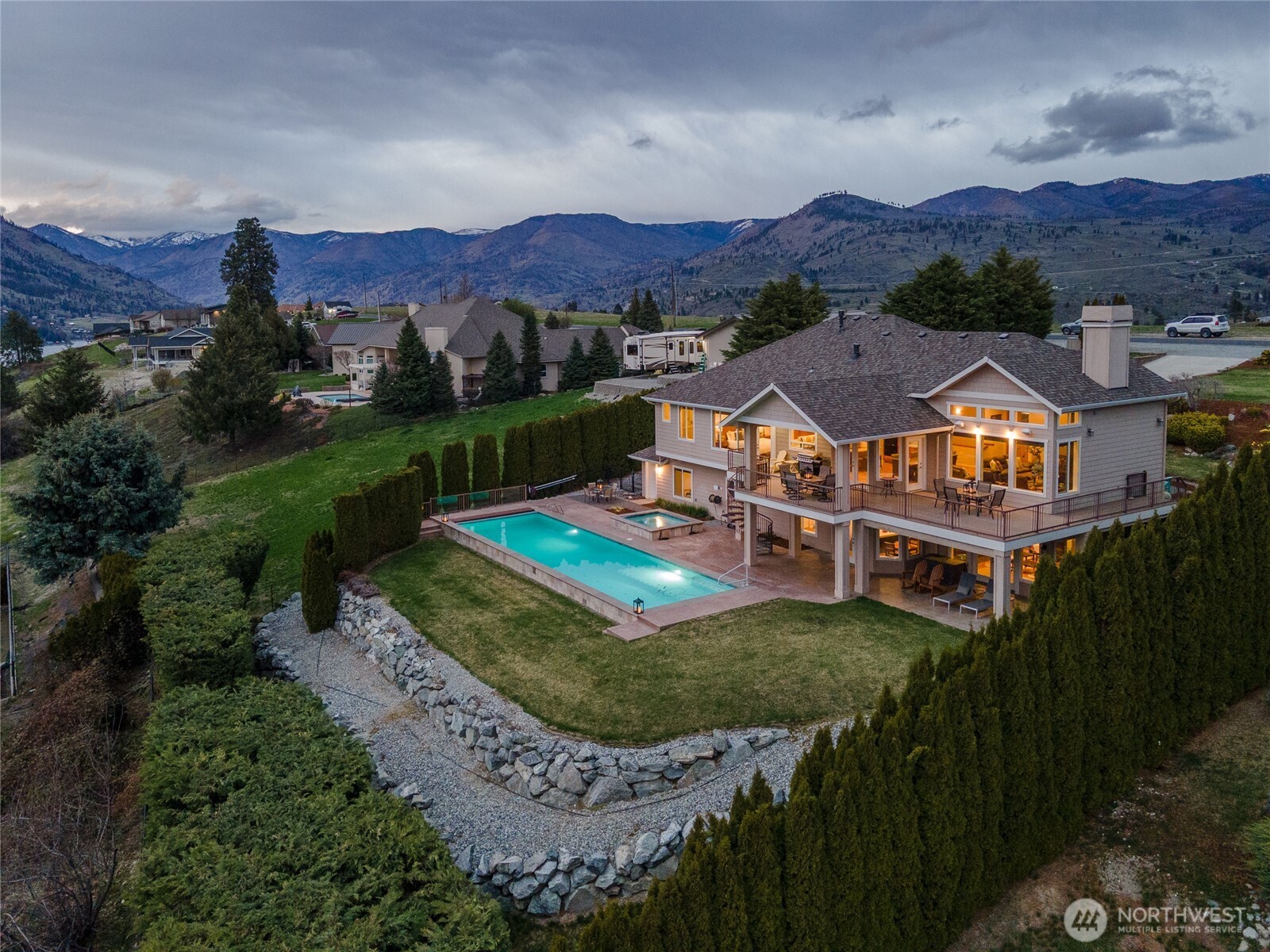 Exterior twilight view of home and landscaping with outdoor living space with oversized heated pool, spa and lounge area.