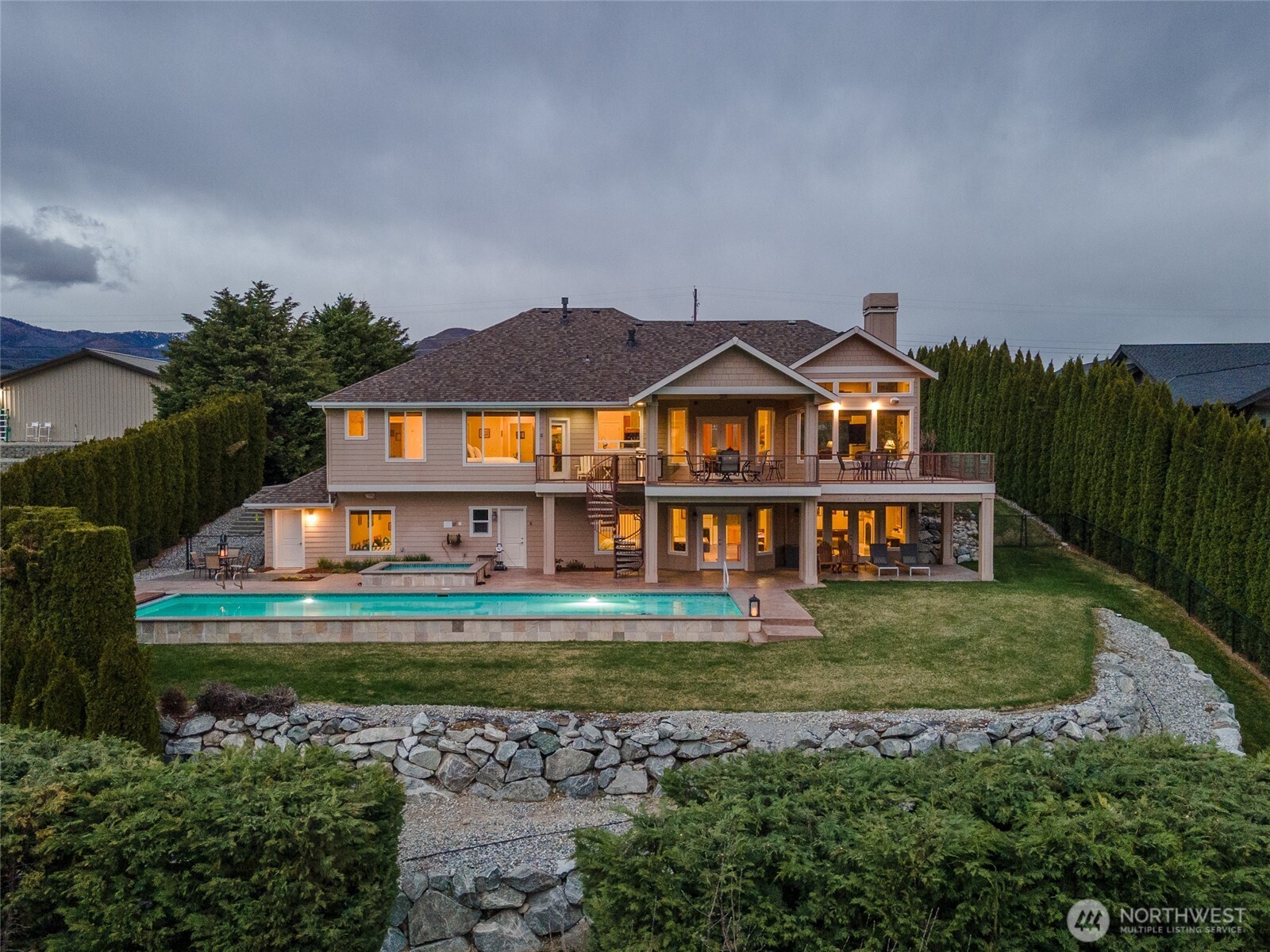 Exterior twilight view 1 of home and outdoor living space with oversized heated pool, spa and lounge area.