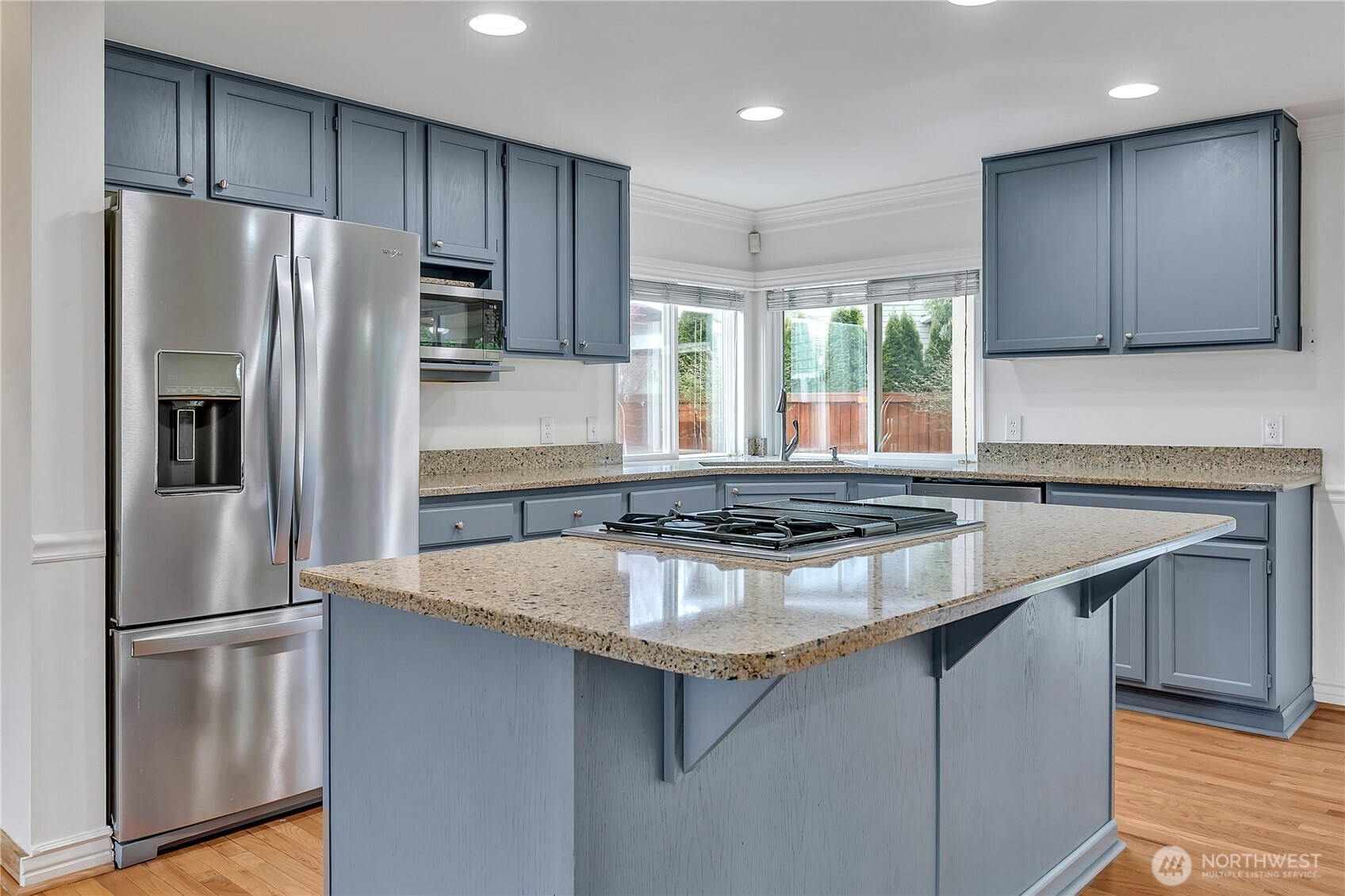 A large eat-up island with cooktop, oven, and stone countertops creates a perfect focal point for the beautiful kitchen.