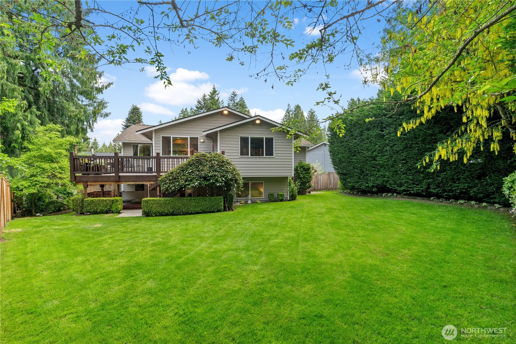 The expansive, level backyard is a tranquil oasis, surrounded by vibrant greenery, mature foliage, and majestic old-growth trees.