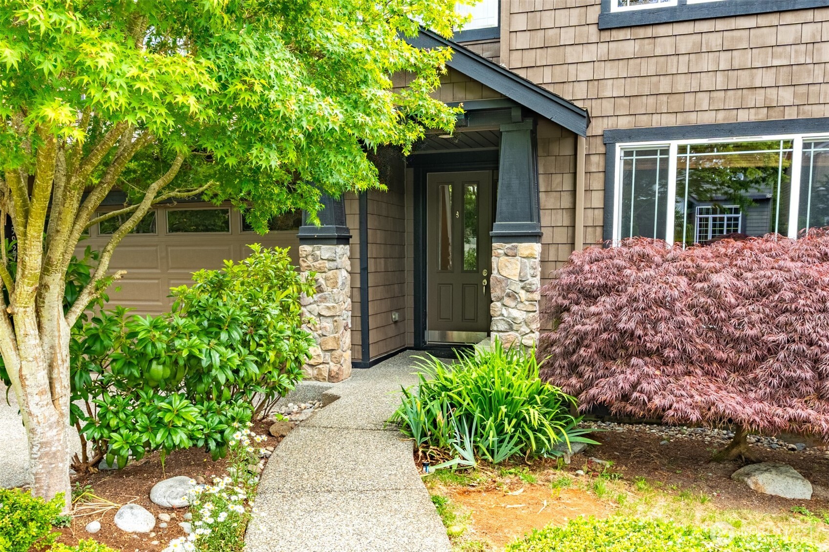 Inviting covered entry framed by stone columns and lush plantings — a warm greeting for you and your guests.