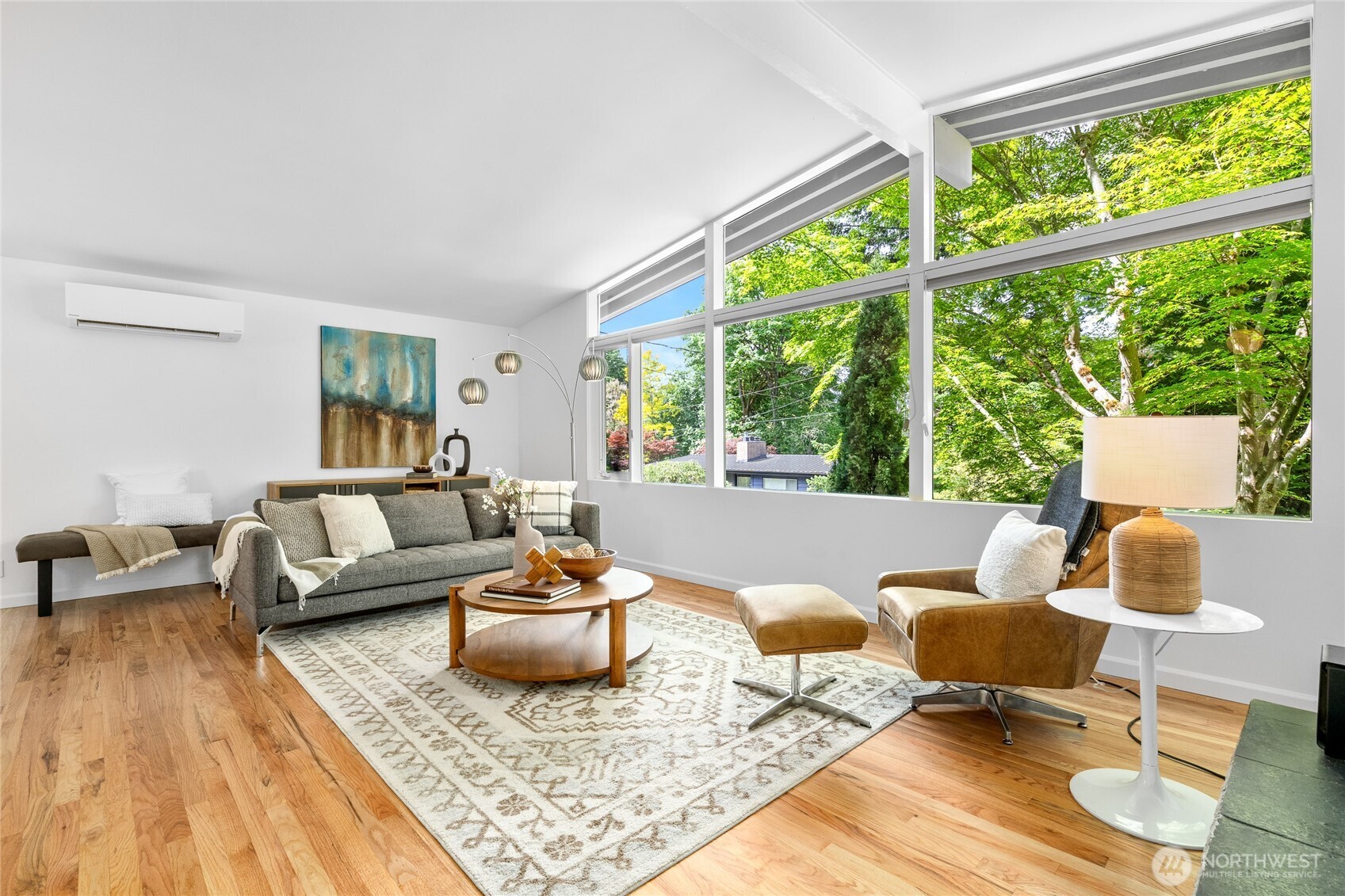 Spacious living room with newly refinished hardwood floors and large west-facing windows that frame the view of the lush surroundings and sunsets. Mid-century details like vaulted ceilings and exposed beams throughout.