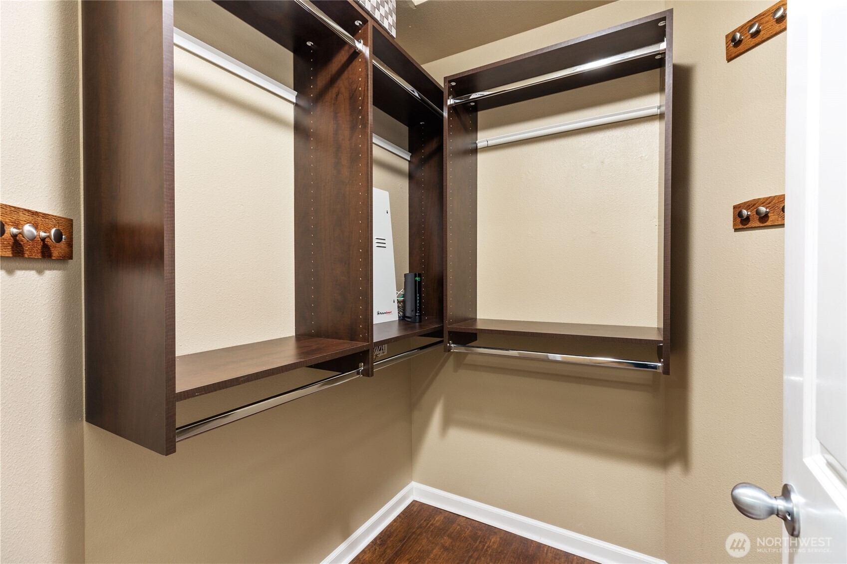 Spacious walk-in closet with custom dark wood built-ins, open shelving and ample hanging space. Includes wall hooks and rich wood flooring.