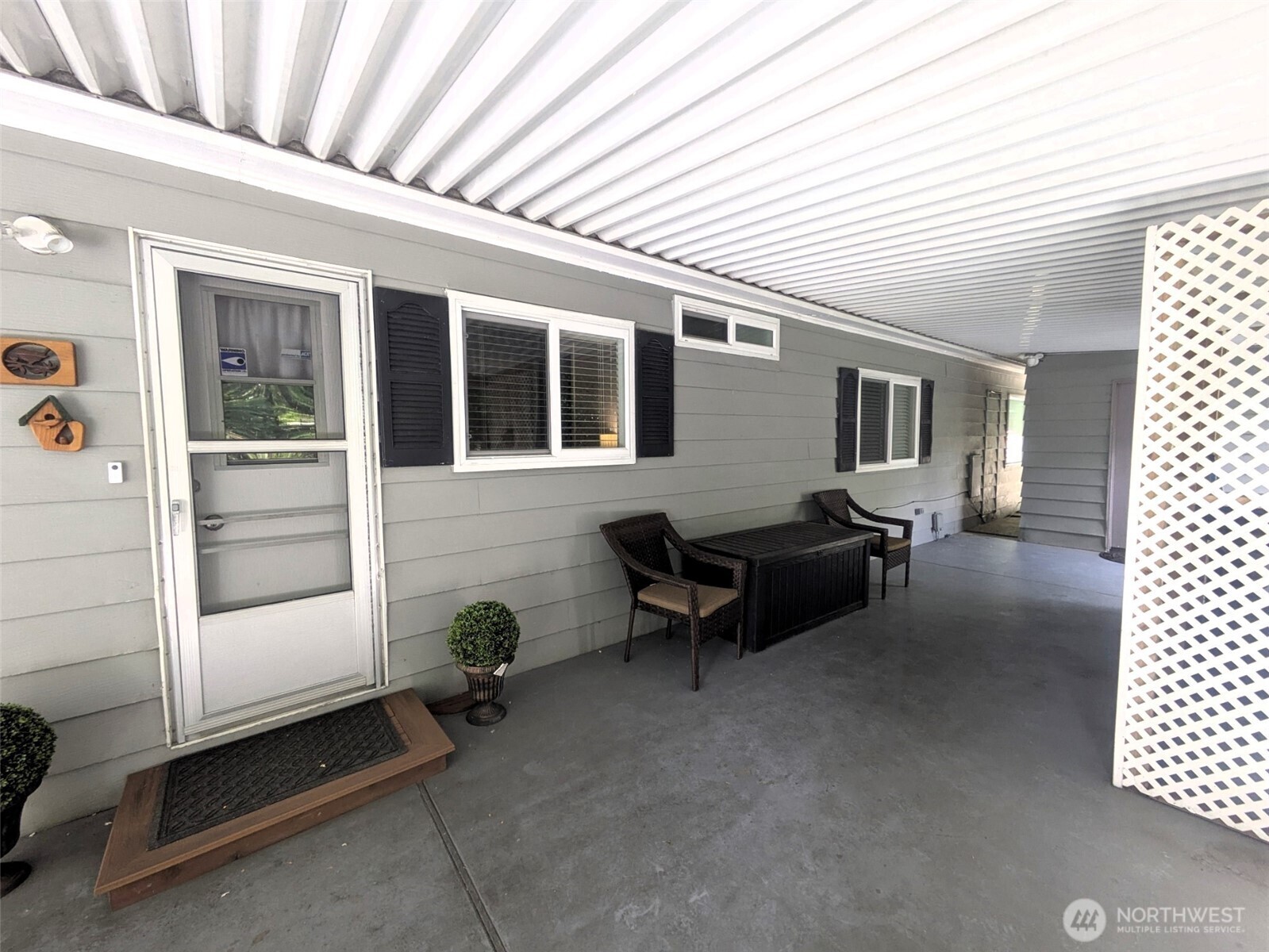End of carport with storage door partially showing and partition for garbage and recycle cans.