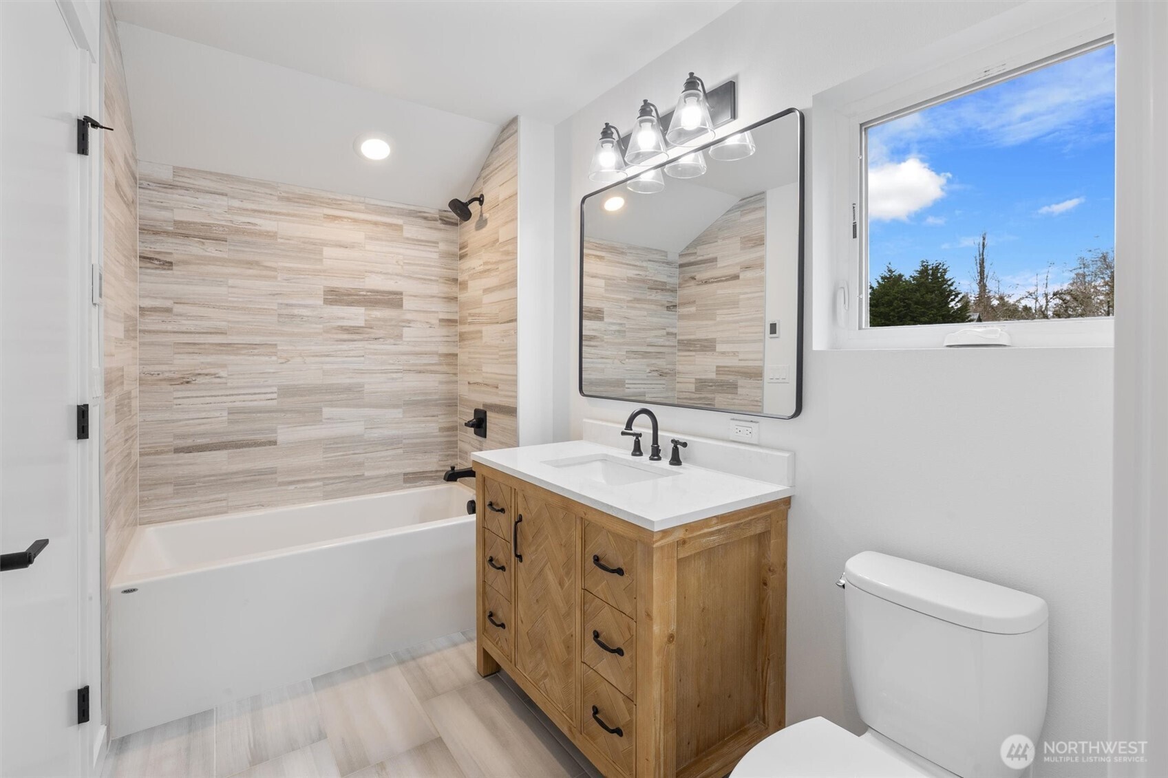 The spa-inspired bath features a rich wood vanity, matte black fixtures, and full-height wood-look tile surround.