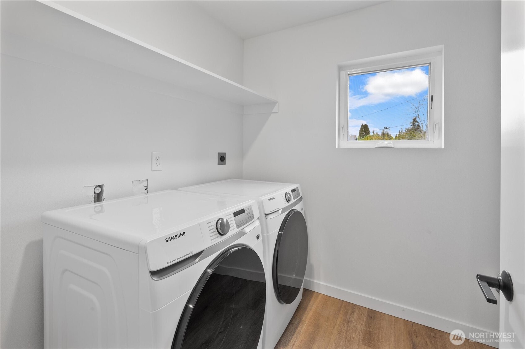 A bright and functional laundry room with Samsung washer and dryer, open shelving, and a picture window.