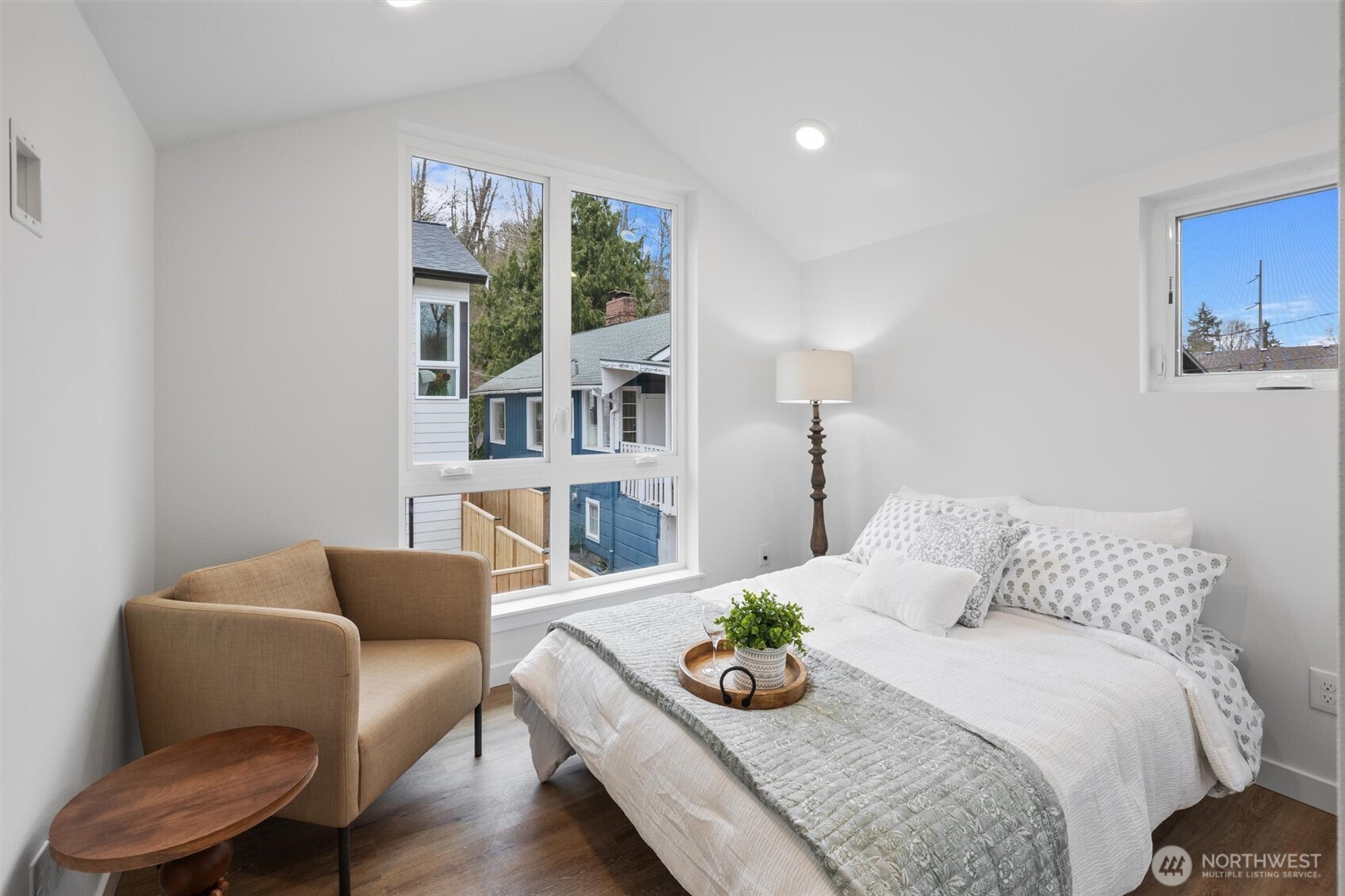 A sunlit secondary bedroom offers serene views through oversized windows and a cozy reading nook.
