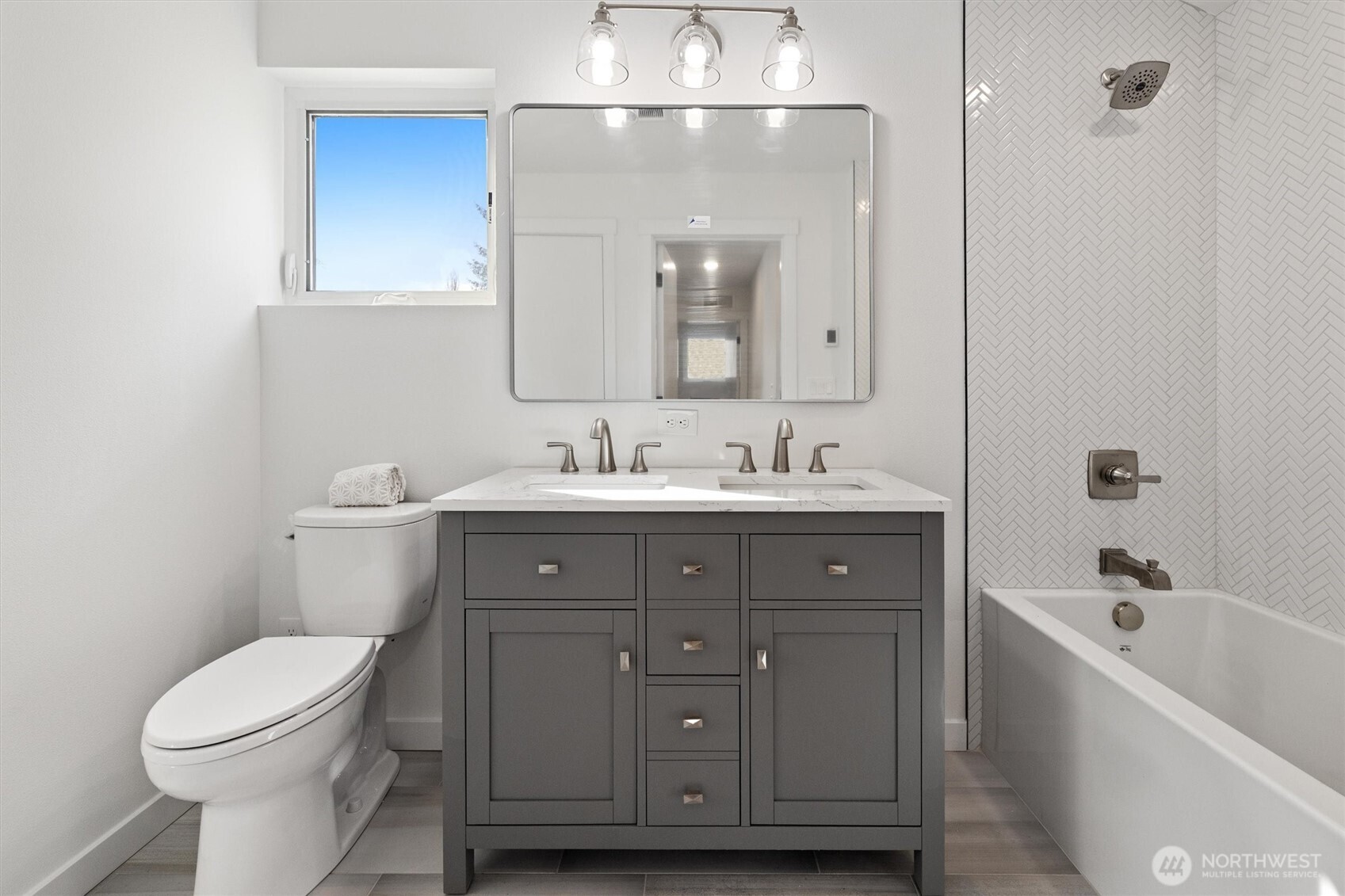 A modern double-sink vanity and herringbone tile shower wall create a stylish and functional bathroom retreat.