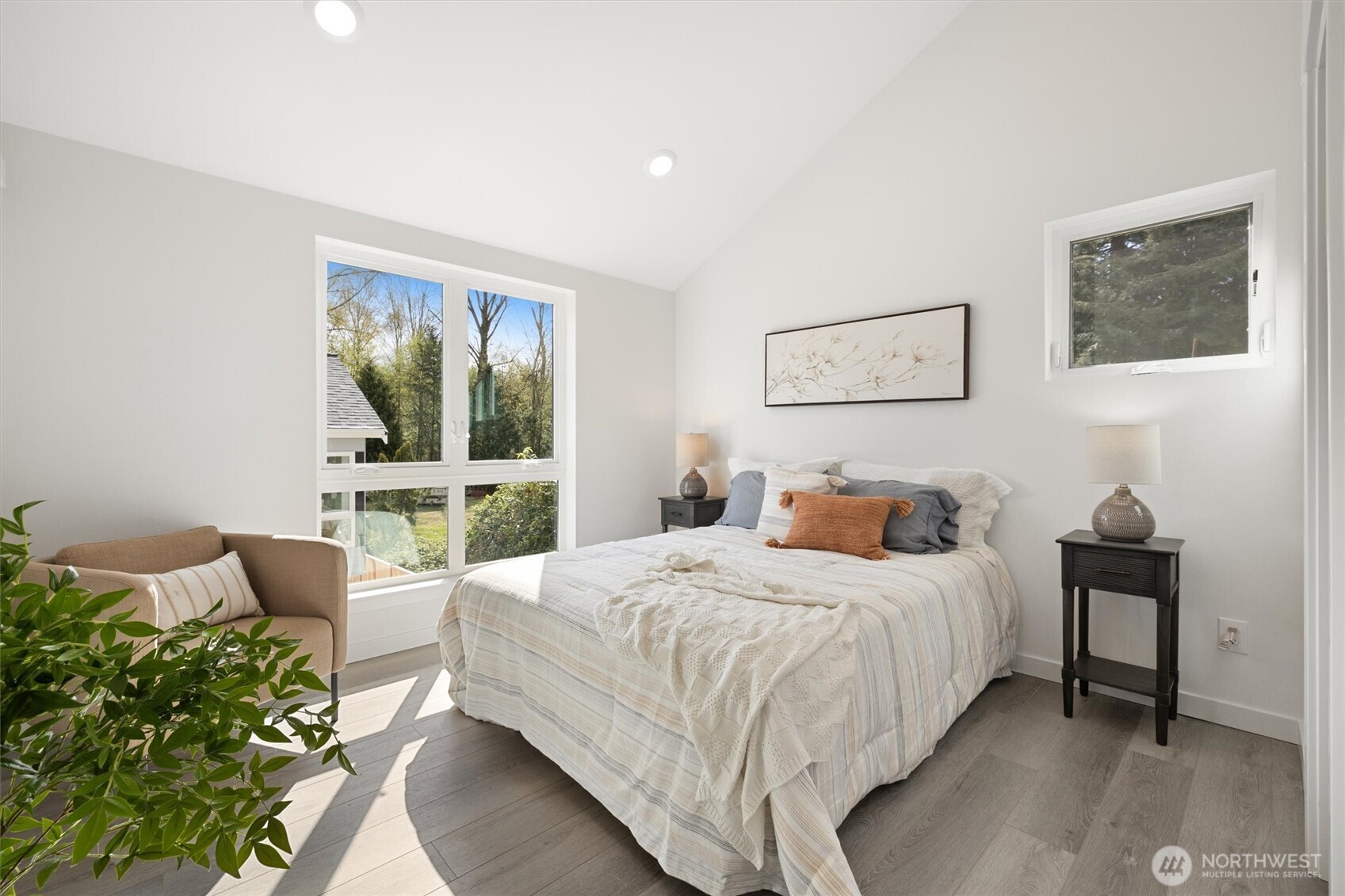 The vaulted-ceiling primary bedroom is a serene retreat featuring picture windows with lush green views and abundant natural light.