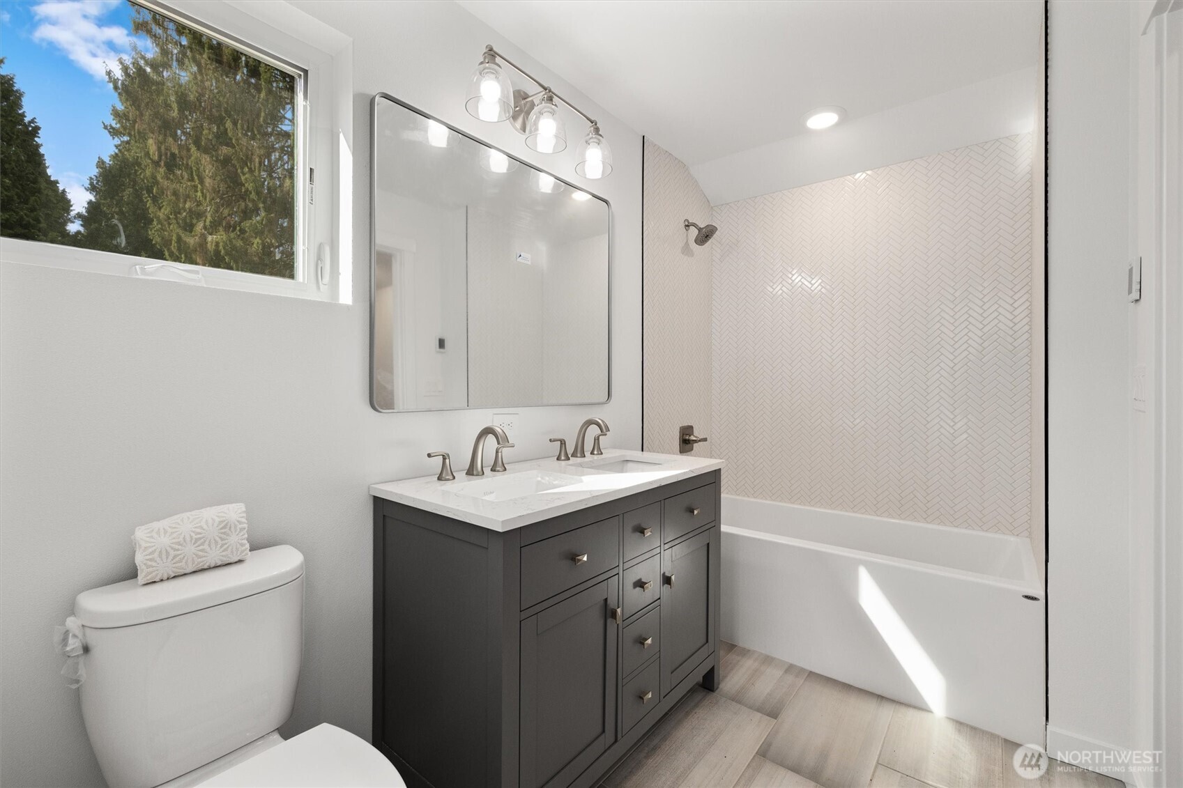 A spa-inspired bathroom features a double vanity, elegant fixtures, and a full-height herringbone tile surround for a polished finish.
