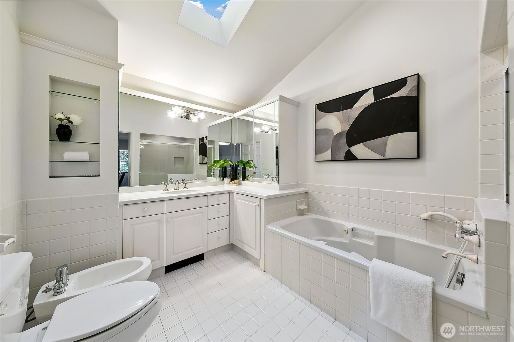 Spa-like en-suite bath featuring a dual vanity, expansive soaking tub beneath a skylight, and a frameless glass shower for serene retreat.