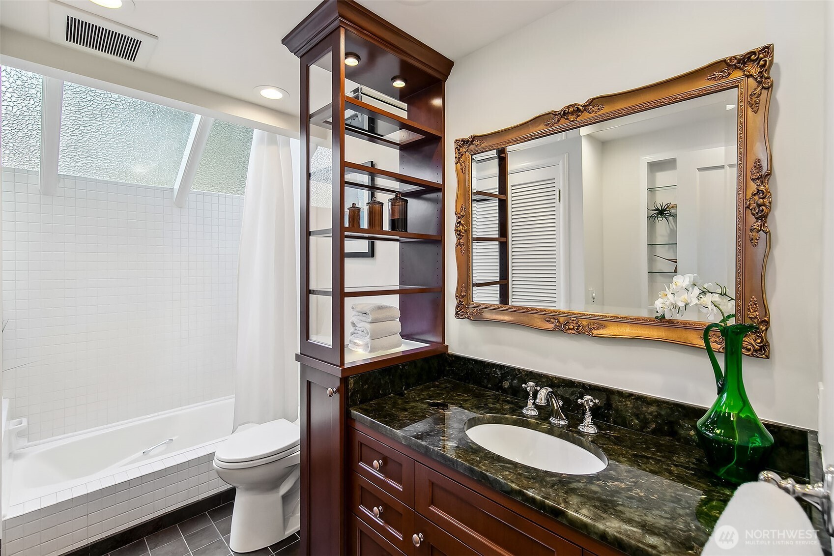 Well-appointed main-level bath featuring a skylit tub/shower, granite-topped vanity and classic tile accents—where natural light enhances daily rituals.