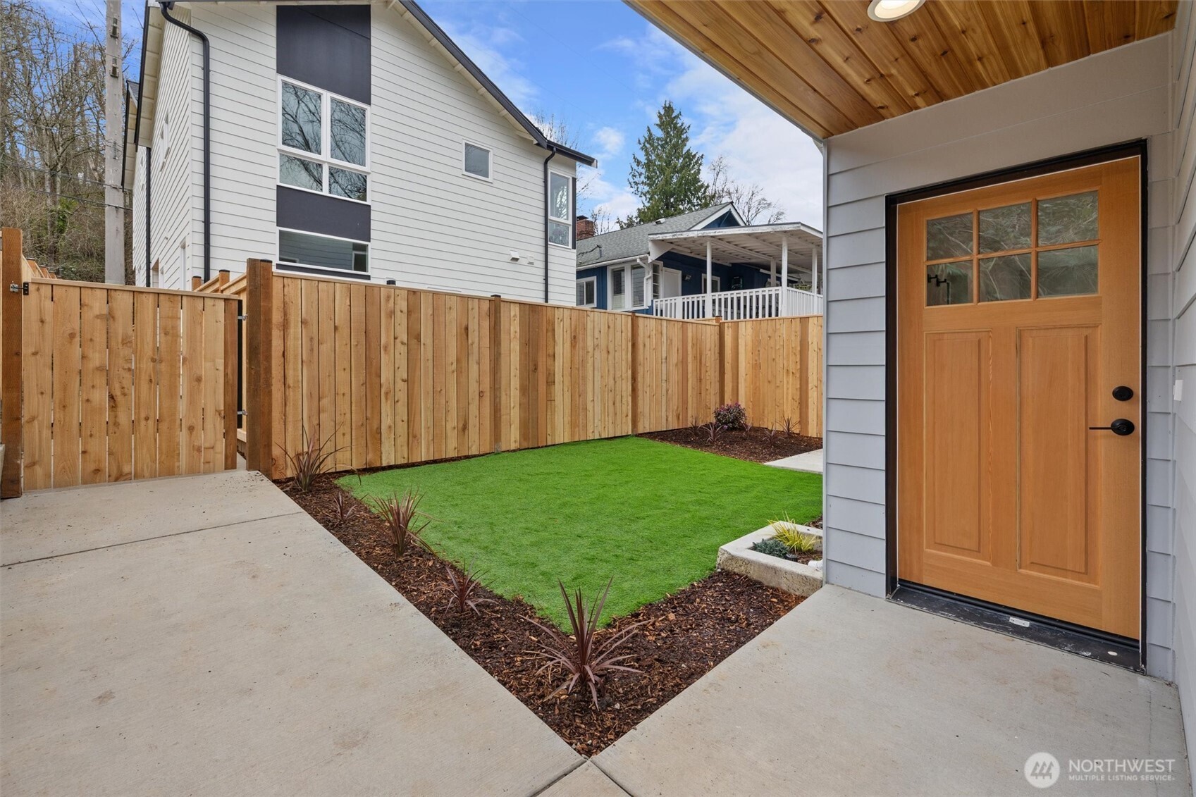 A covered entry opens to a private, fully fenced yard with fresh landscaping and durable turf for year-round greenery.
