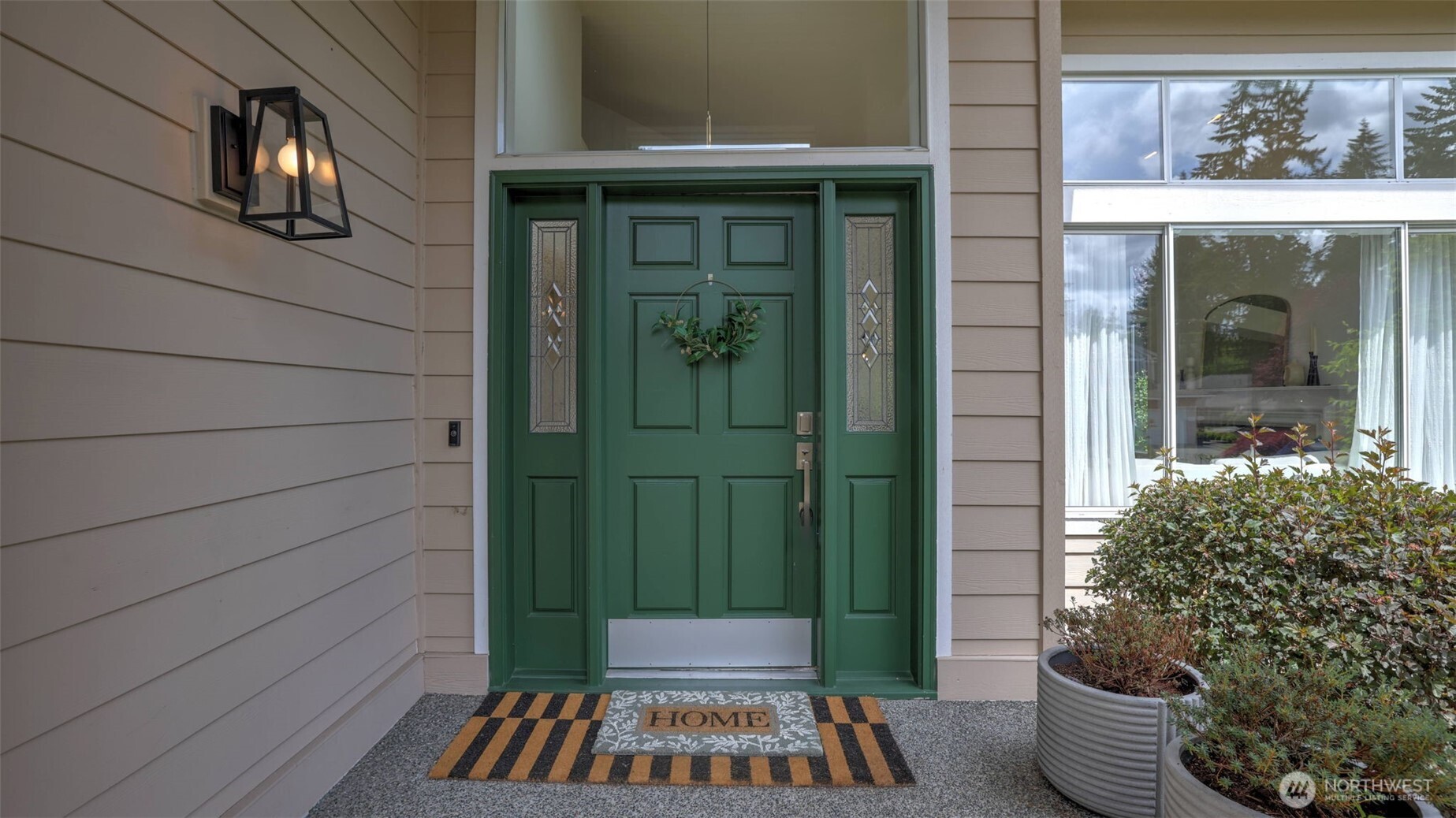 The inviting entrance features a bold green front door framed by surrounding windows and lush greenery, setting a warm and vibrant tone for the home