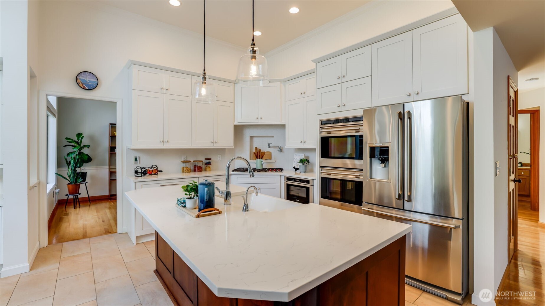 Featuring a colossal island with gleaming quartz countertops, sleek tile flooring, a striking black tile backsplash, and soaring ceilings that enhance the open, airy ambiance